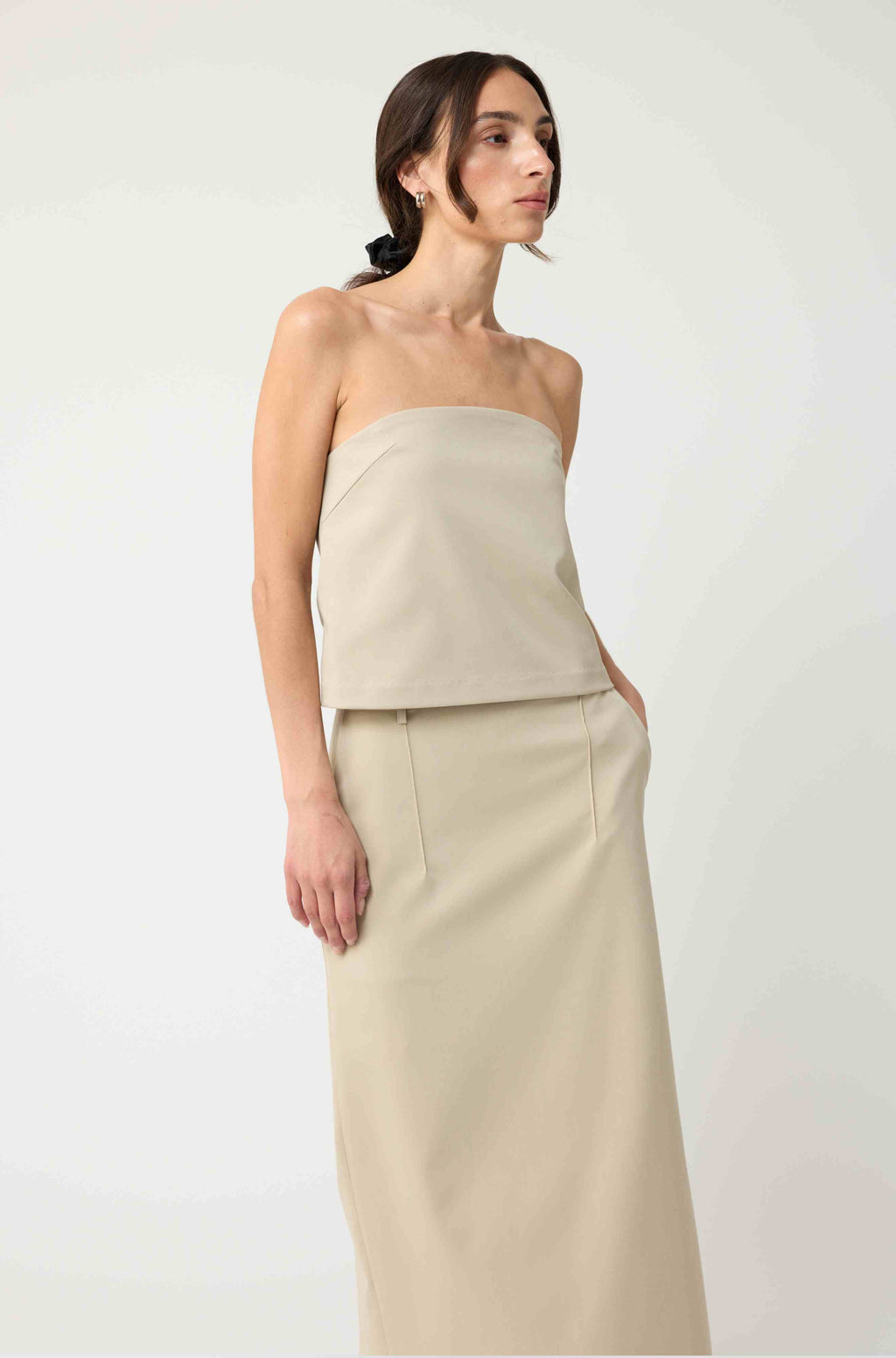 Woman wearing a beige strapless top with a matching beige skirt on a light grey background