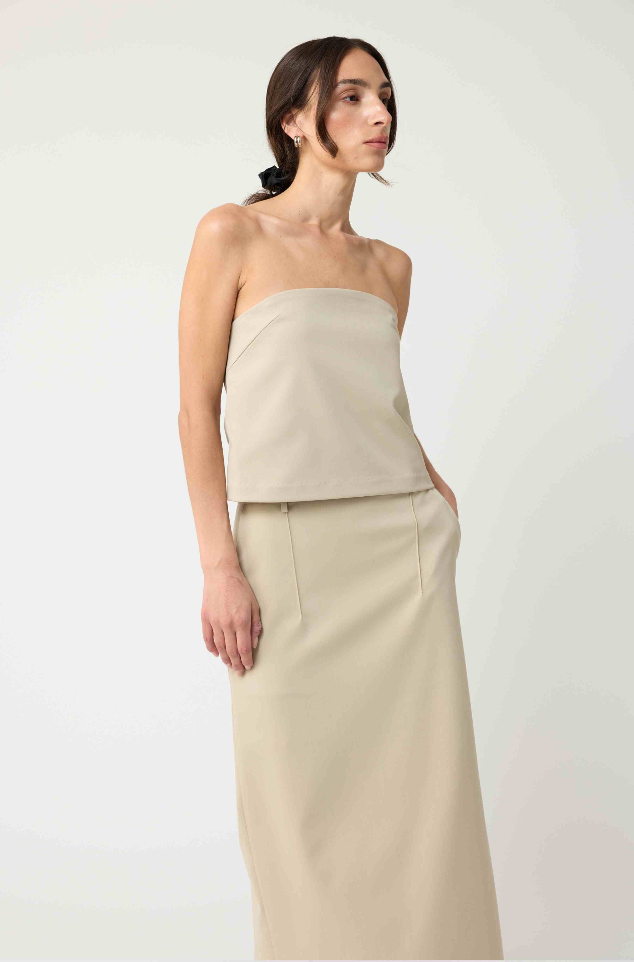 Woman wearing a beige strapless top with a matching beige skirt on a light grey background