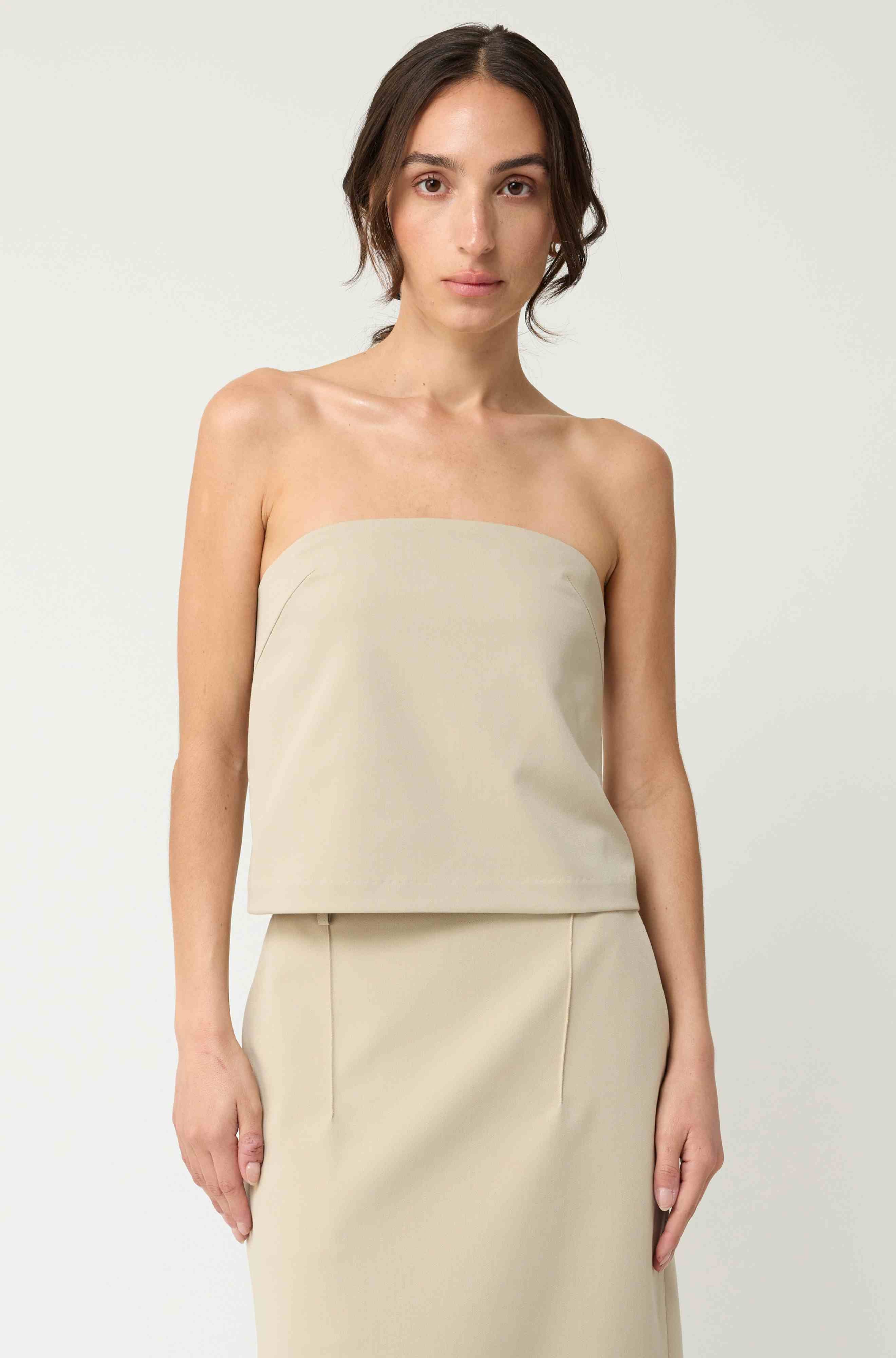 Woman wearing a beige strapless top with a matching beige skirt on a light grey background