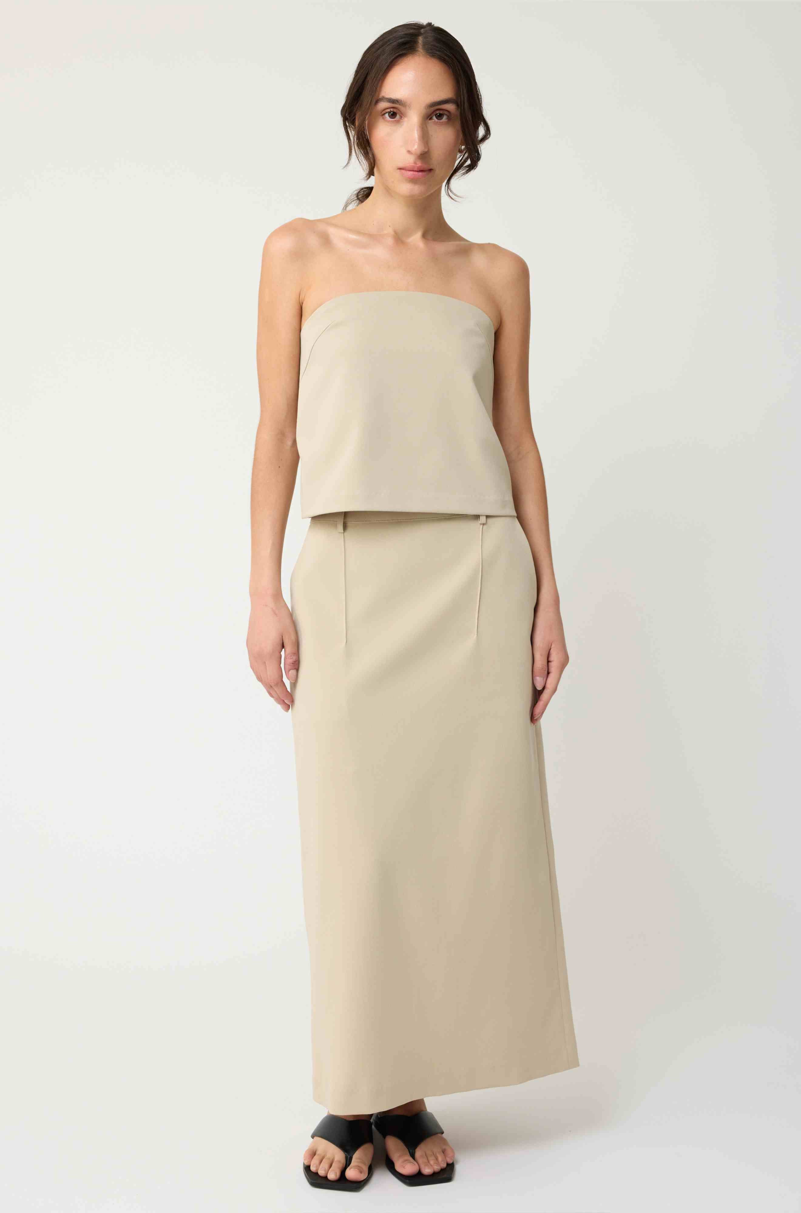 Woman wearing a beige strapless top with a matching beige skirt on a light grey background
