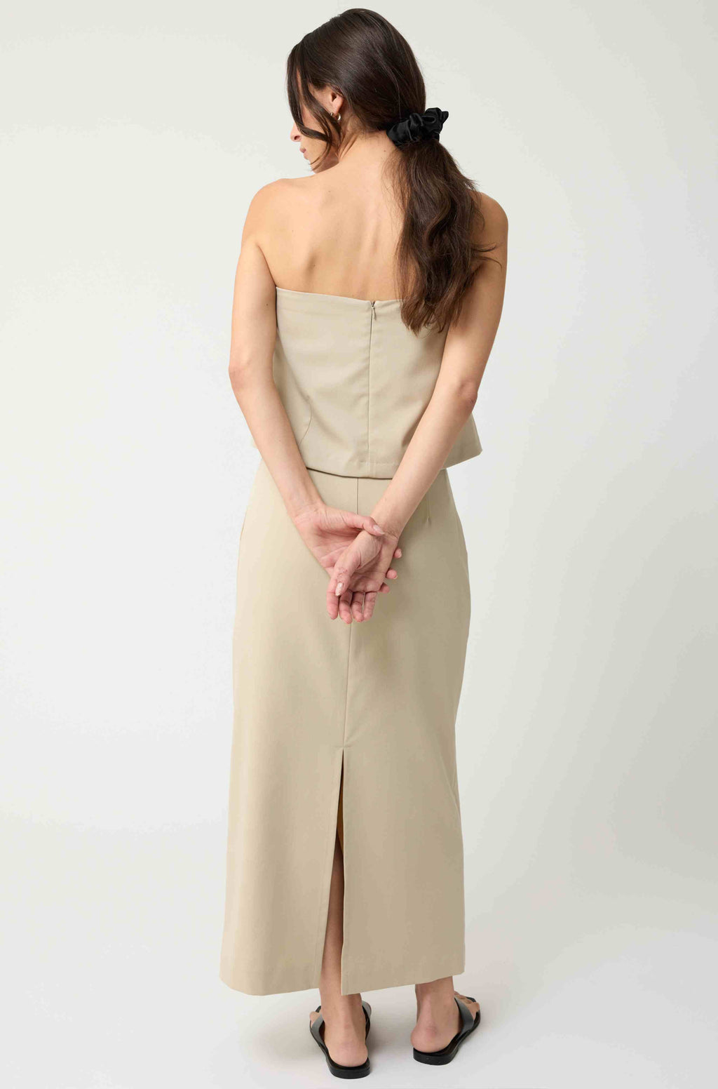 Woman wearing a beige strapless top with a matching beige skirt on a light grey background