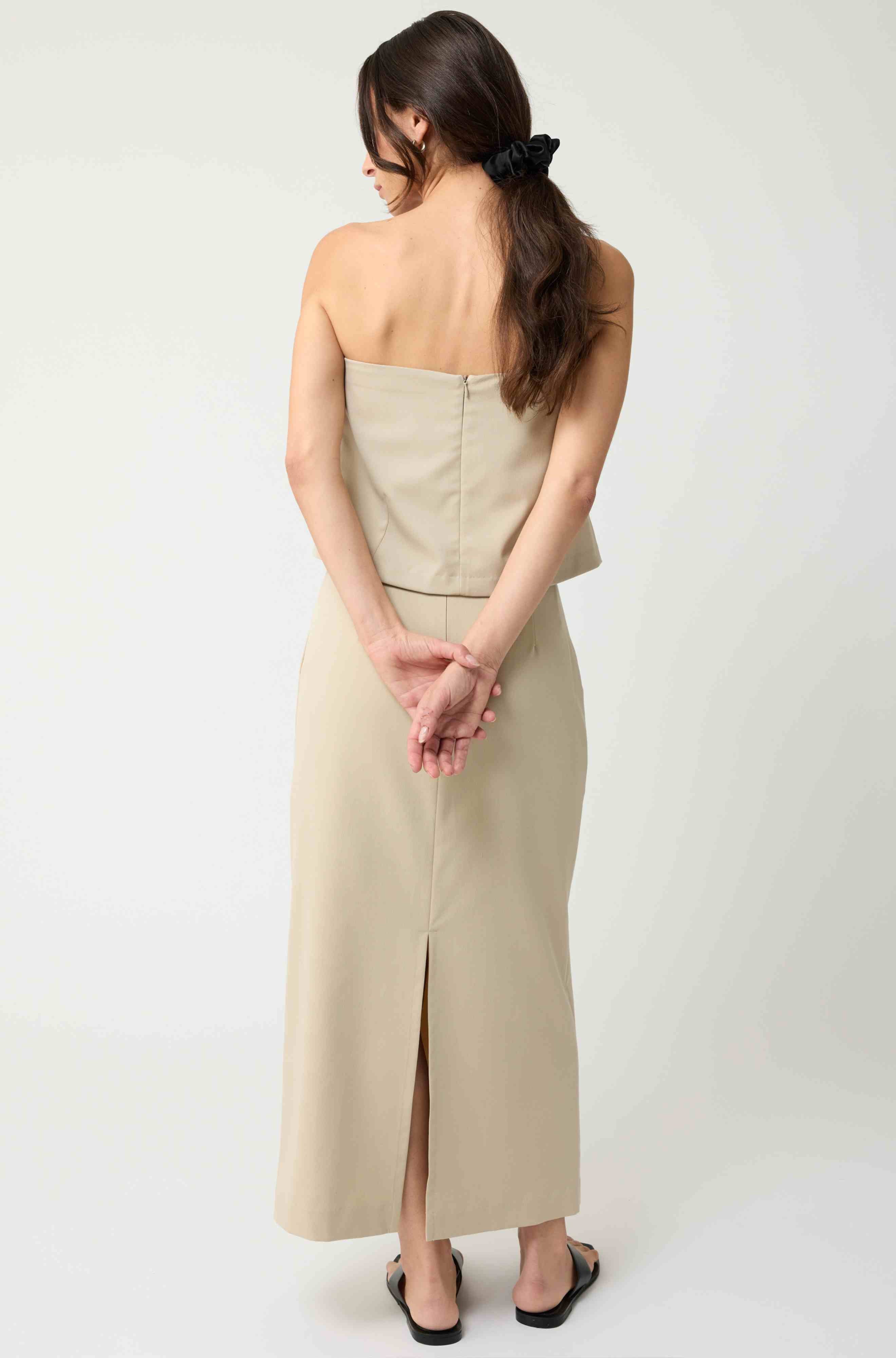 Woman wearing a beige strapless top with a matching beige skirt on a light grey background