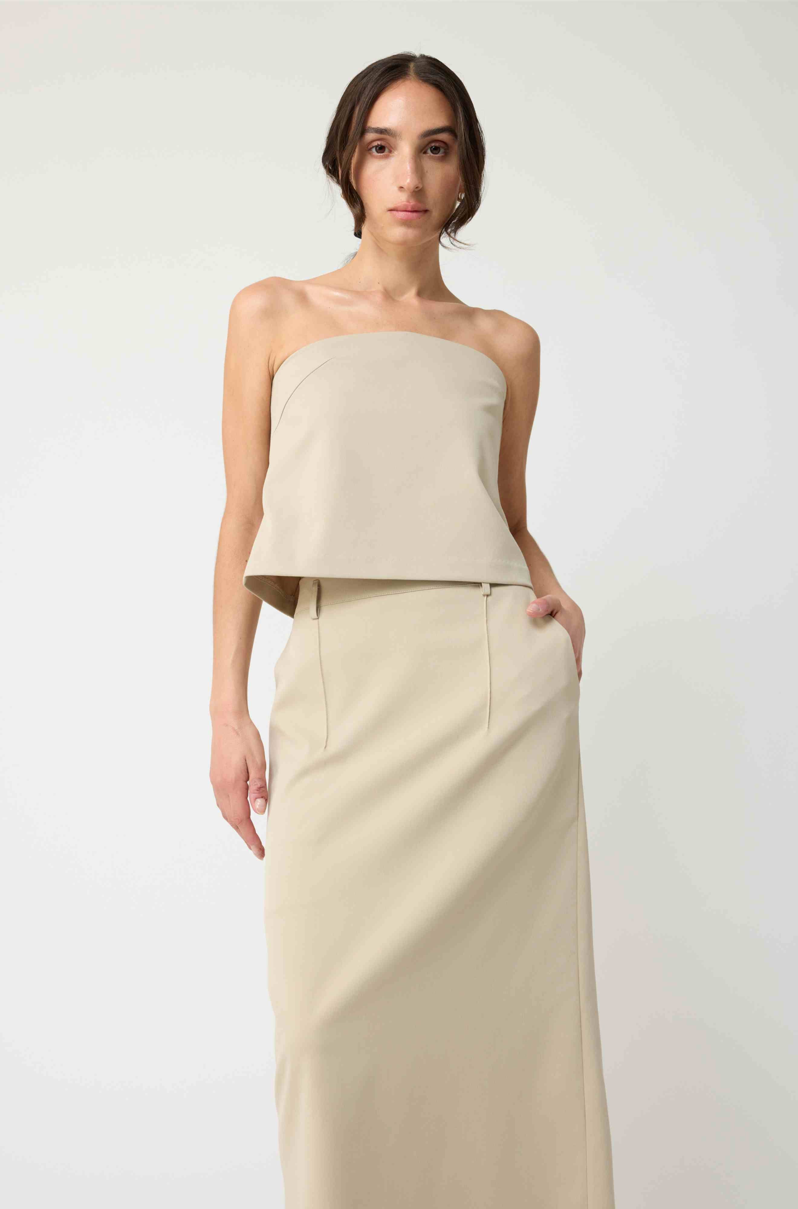 Woman wearing a beige strapless top with a matching beige skirt on a light grey background