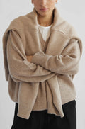 Person wearing a beige cardigan over a white shirt on a light gray background