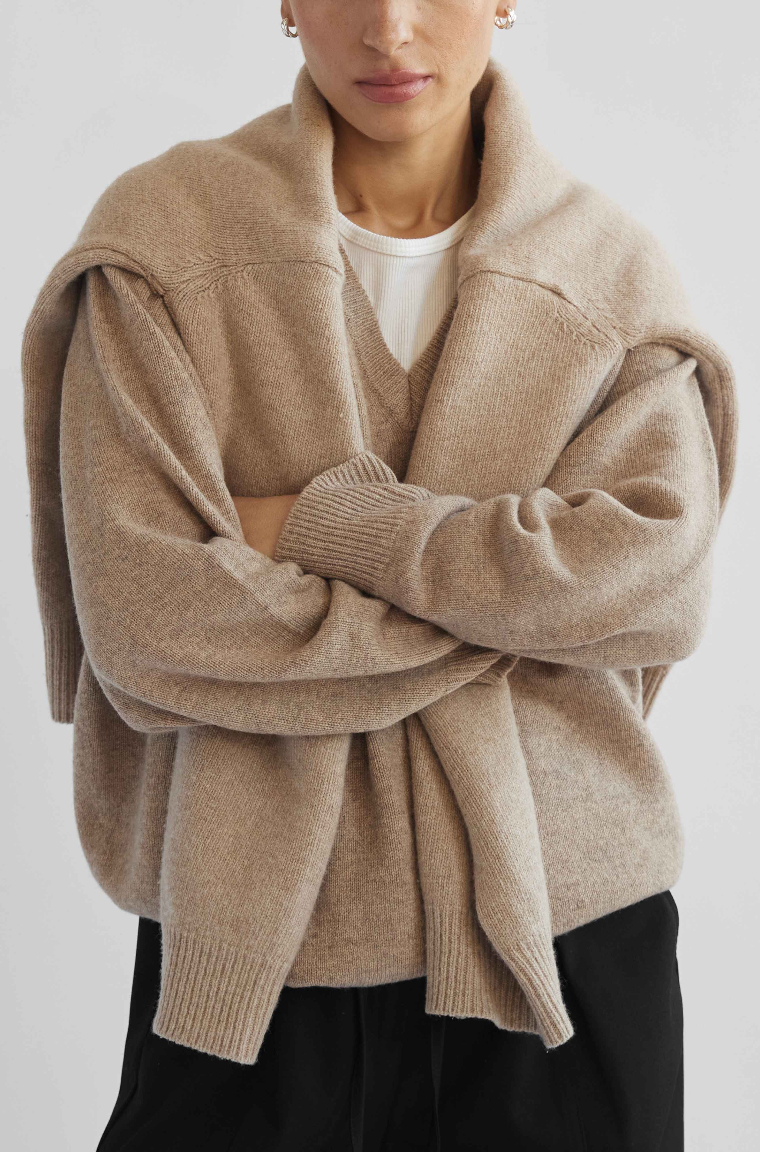 Person wearing a beige cardigan over a white shirt on a light gray background
