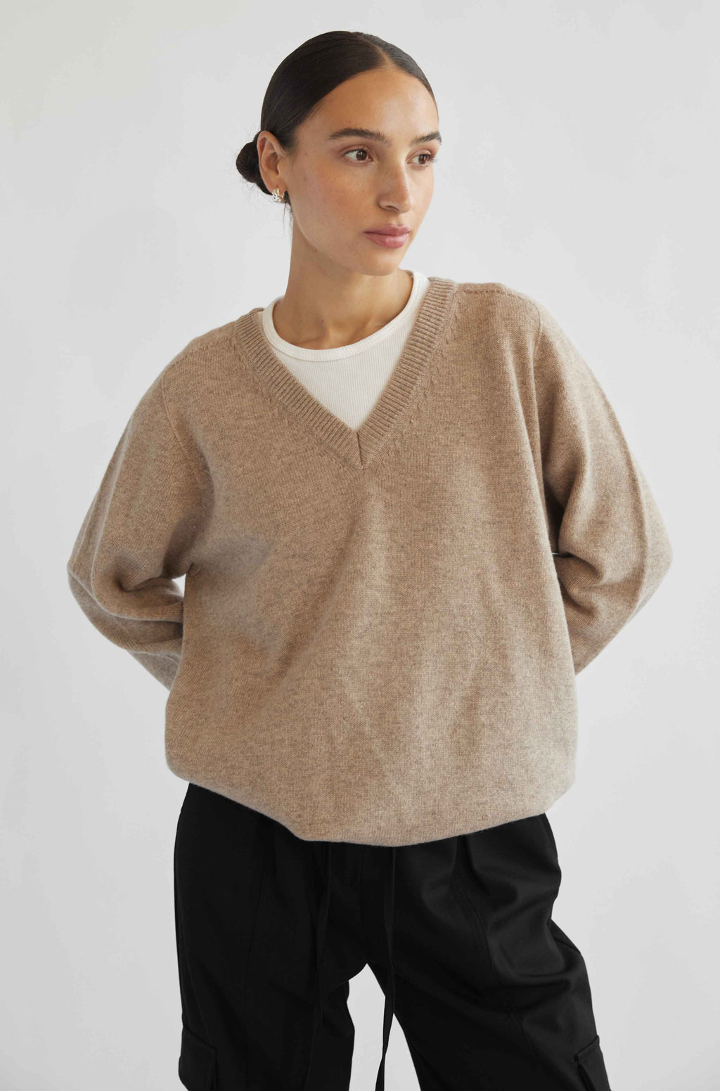 Woman wearing a beige sweater over a white shirt with black pants on a light gray background