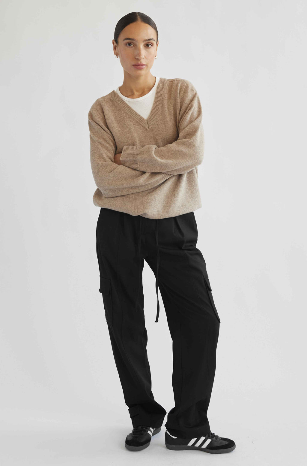 Person wearing a beige sweater and black pants on a white background