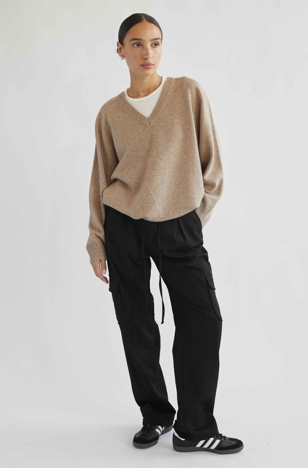 Person wearing a beige sweater and black pants on a white background
