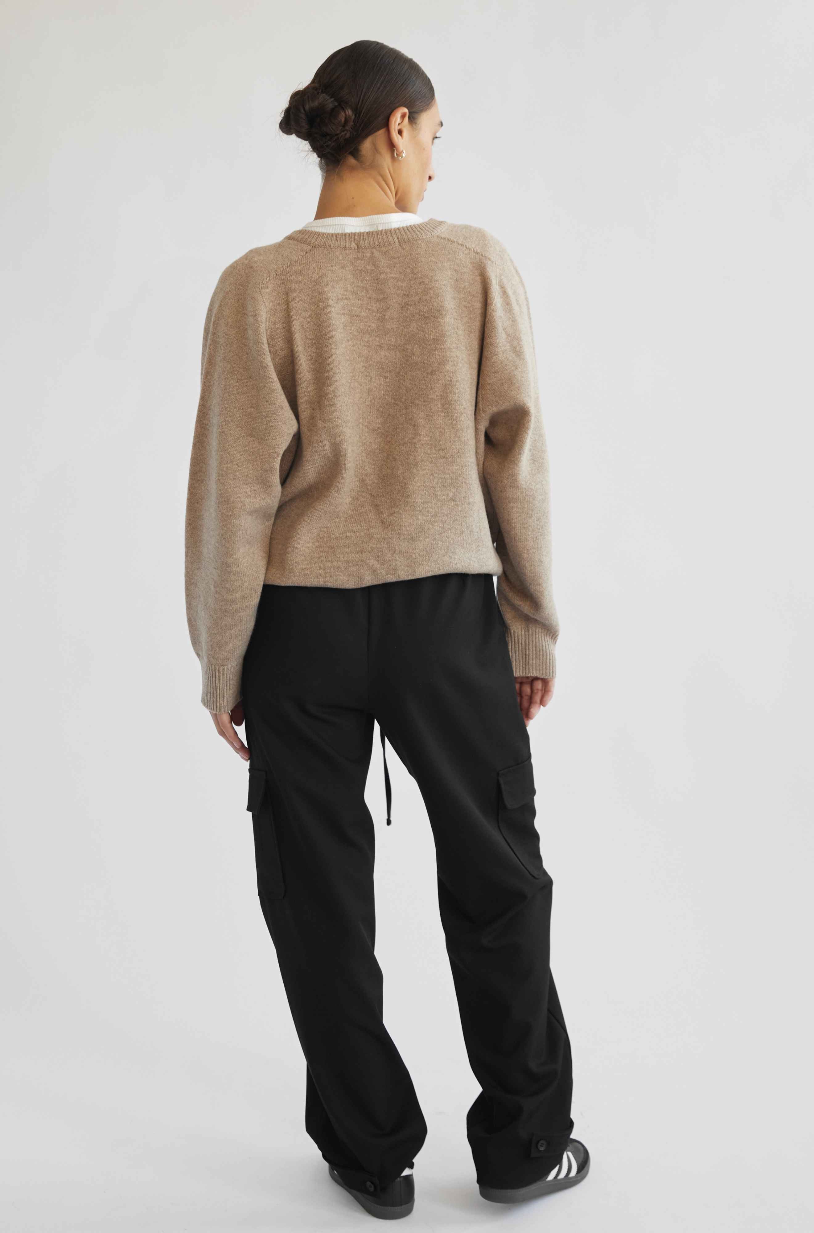 Person wearing a beige sweater and black pants on a white background