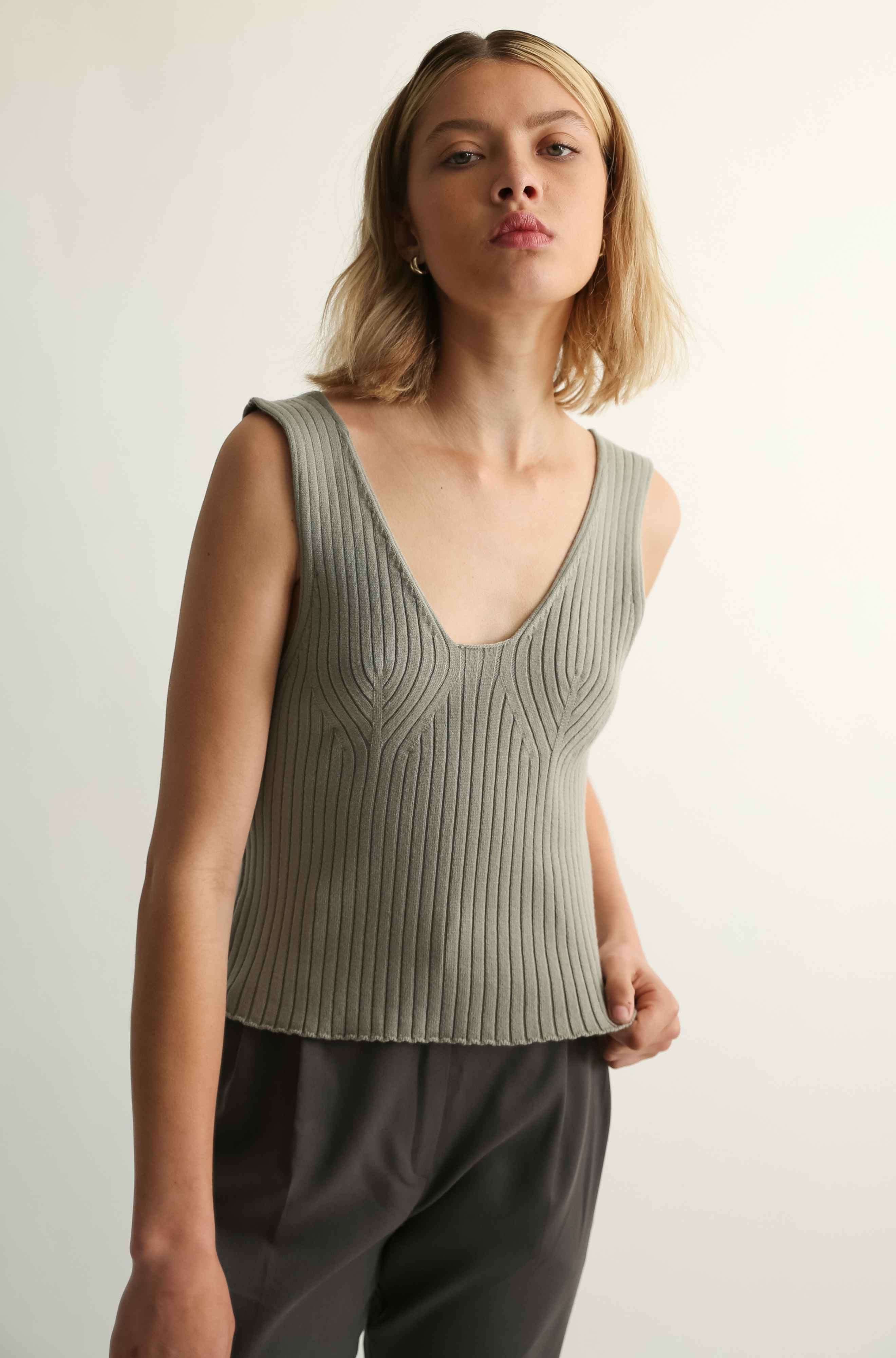 Woman wearing a sleeveless ribbed top and dark pants against a plain background