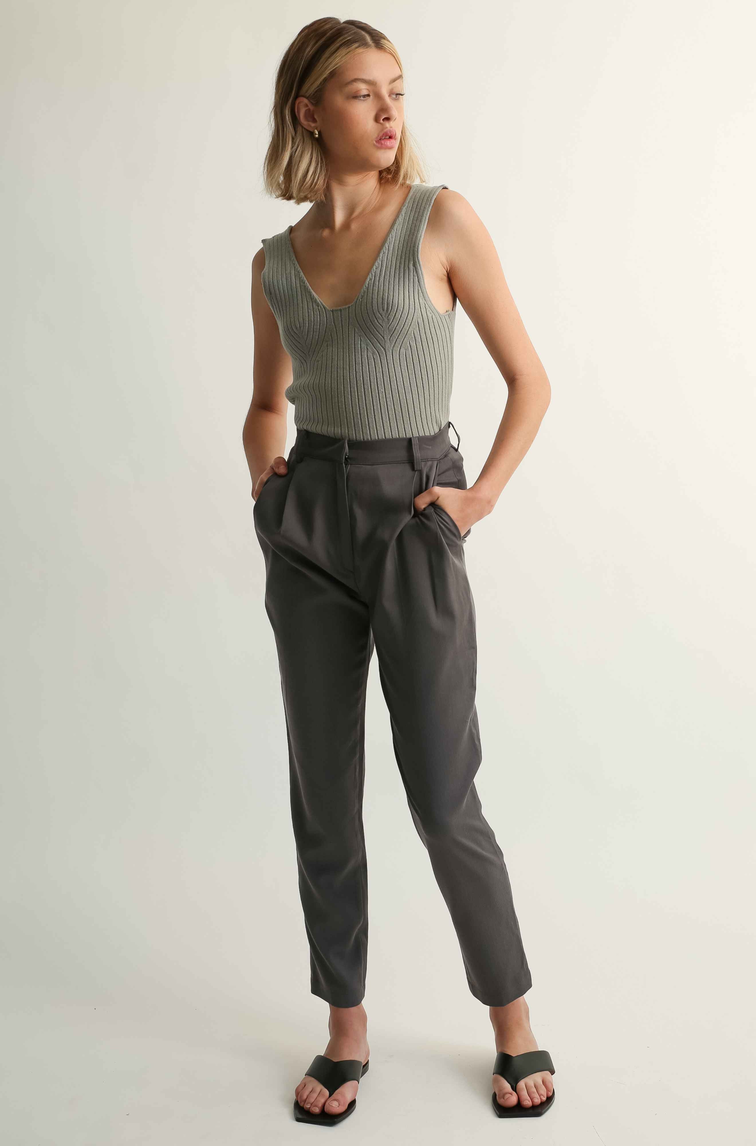 Woman wearing a sleeveless ribbed top and high-waisted pants on a light background