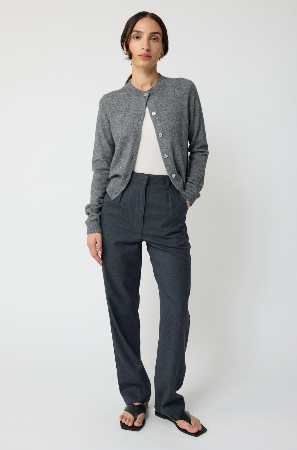 Person wearing a gray cardigan and dark pants on a white background