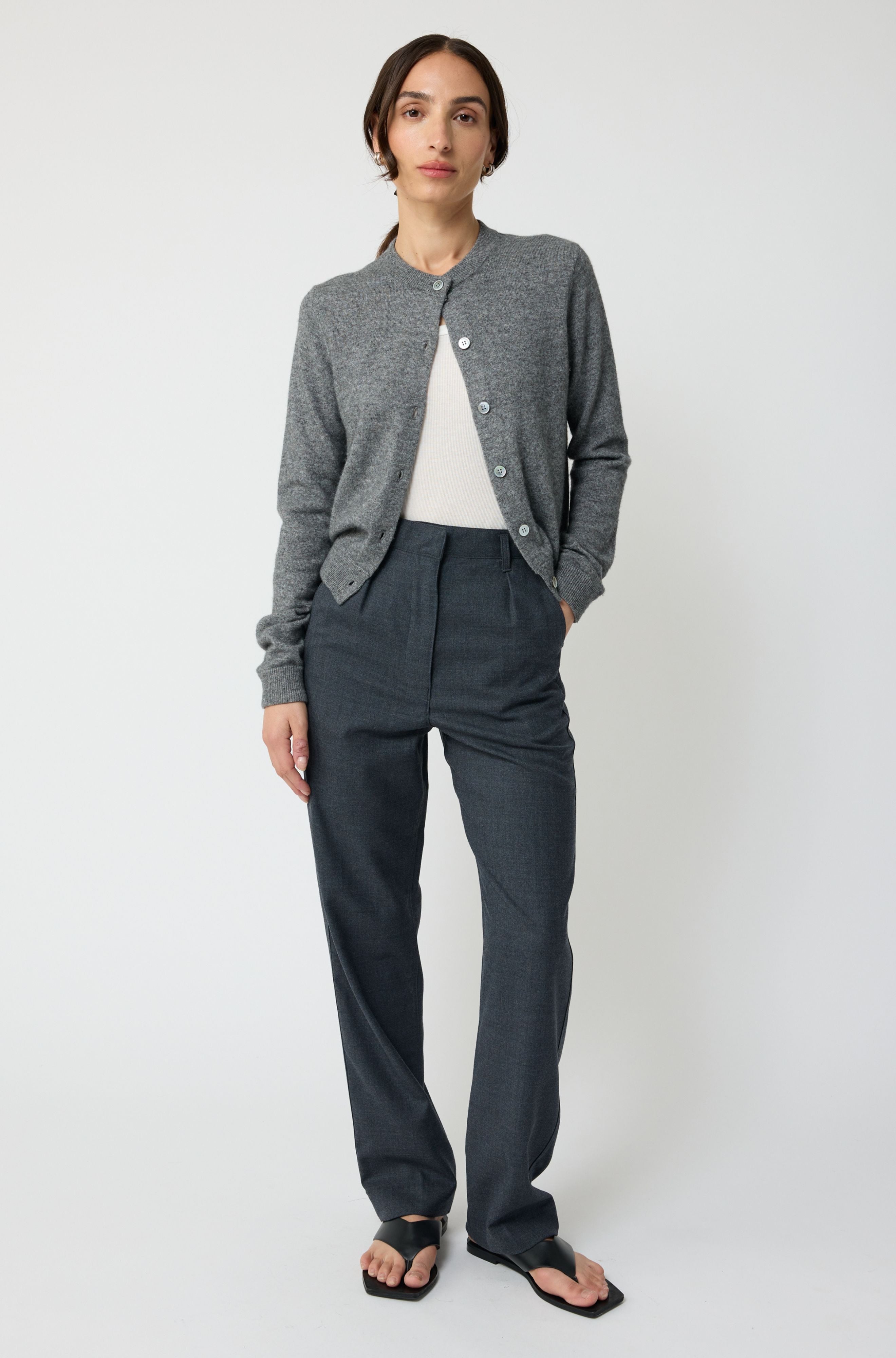 Person wearing a gray cardigan and dark pants on a white background