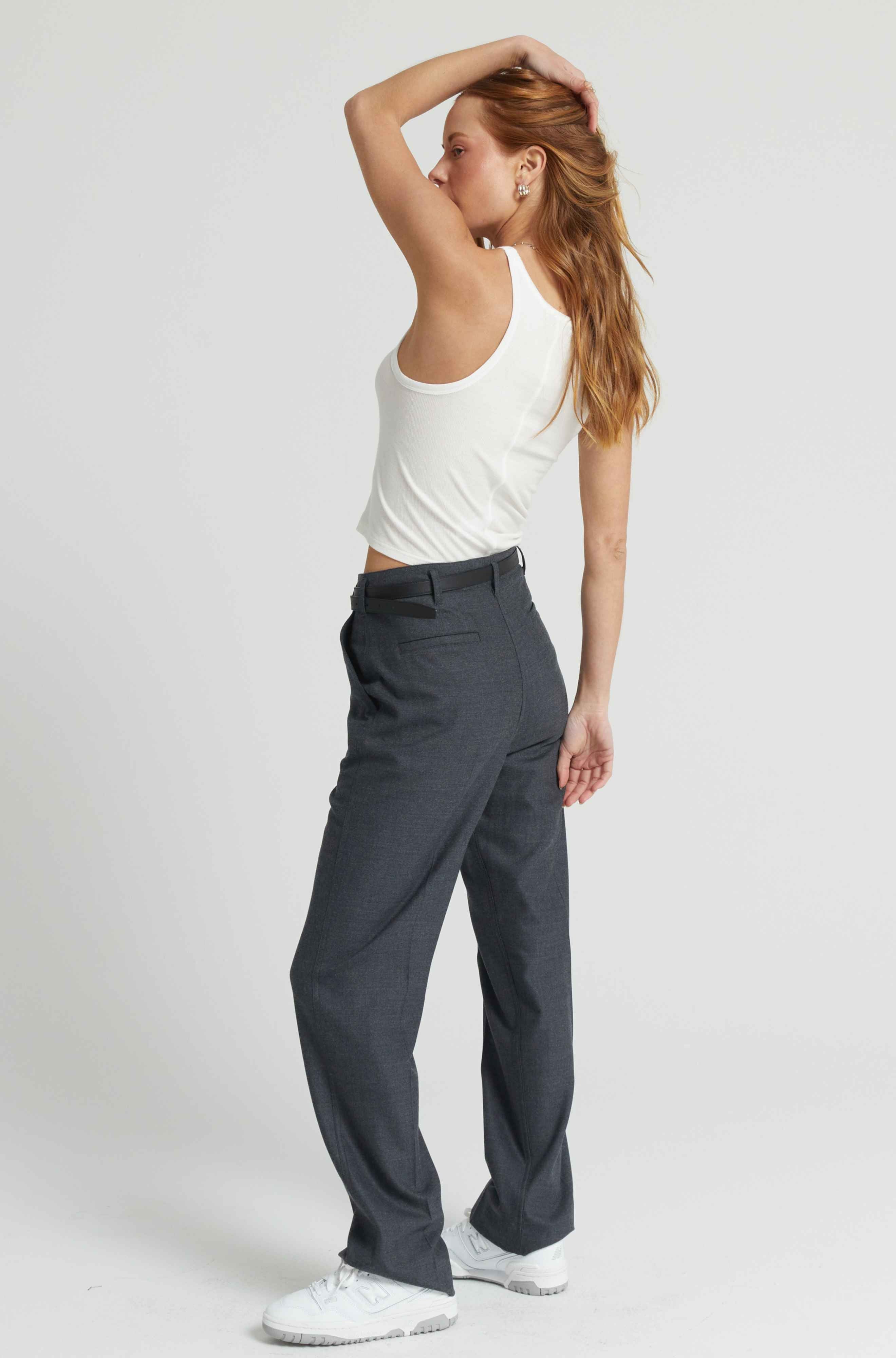 Woman wearing gray pants and a white top on a plain background