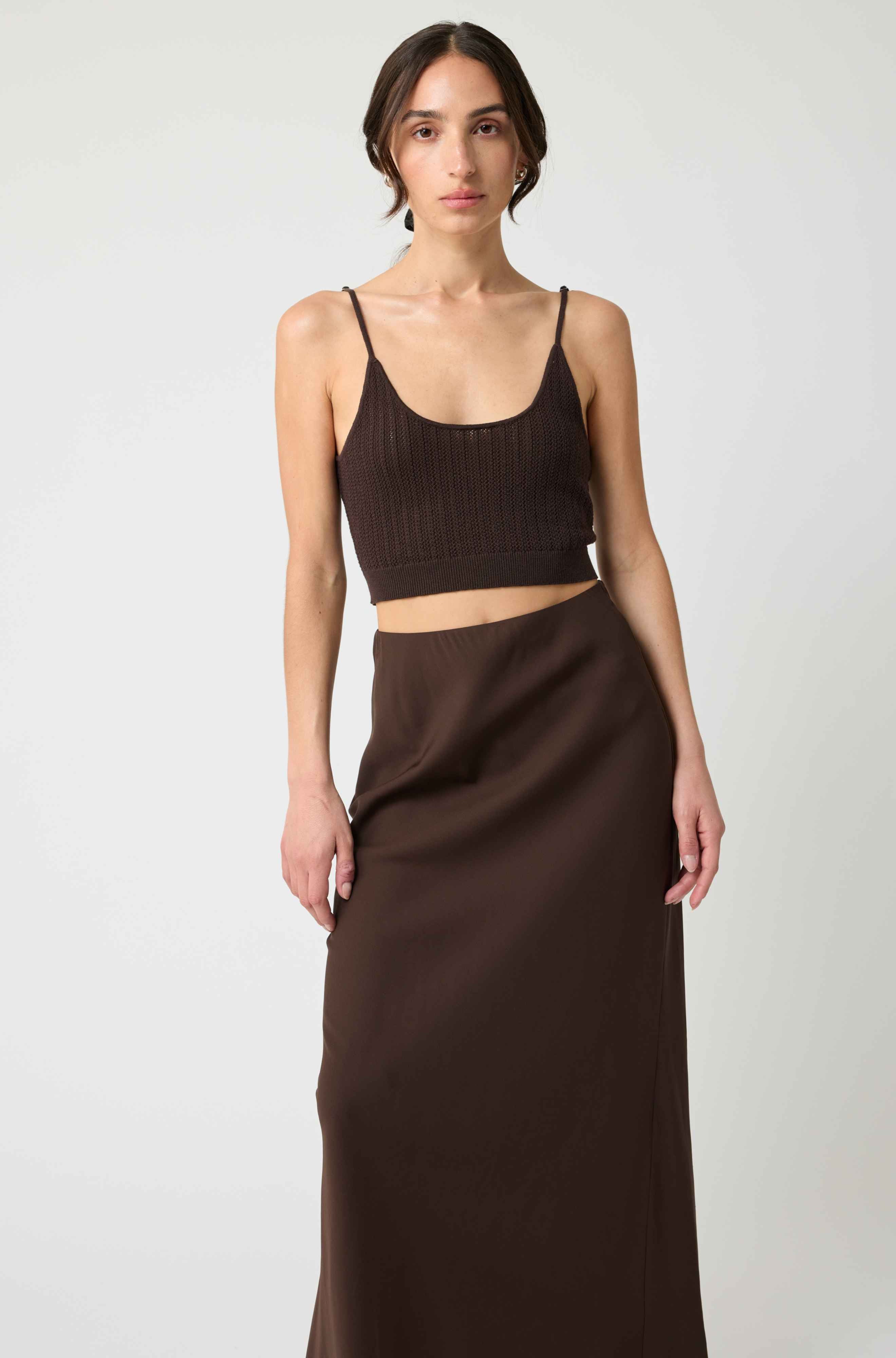 Woman wearing a brown cropped top and long skirt against a white background