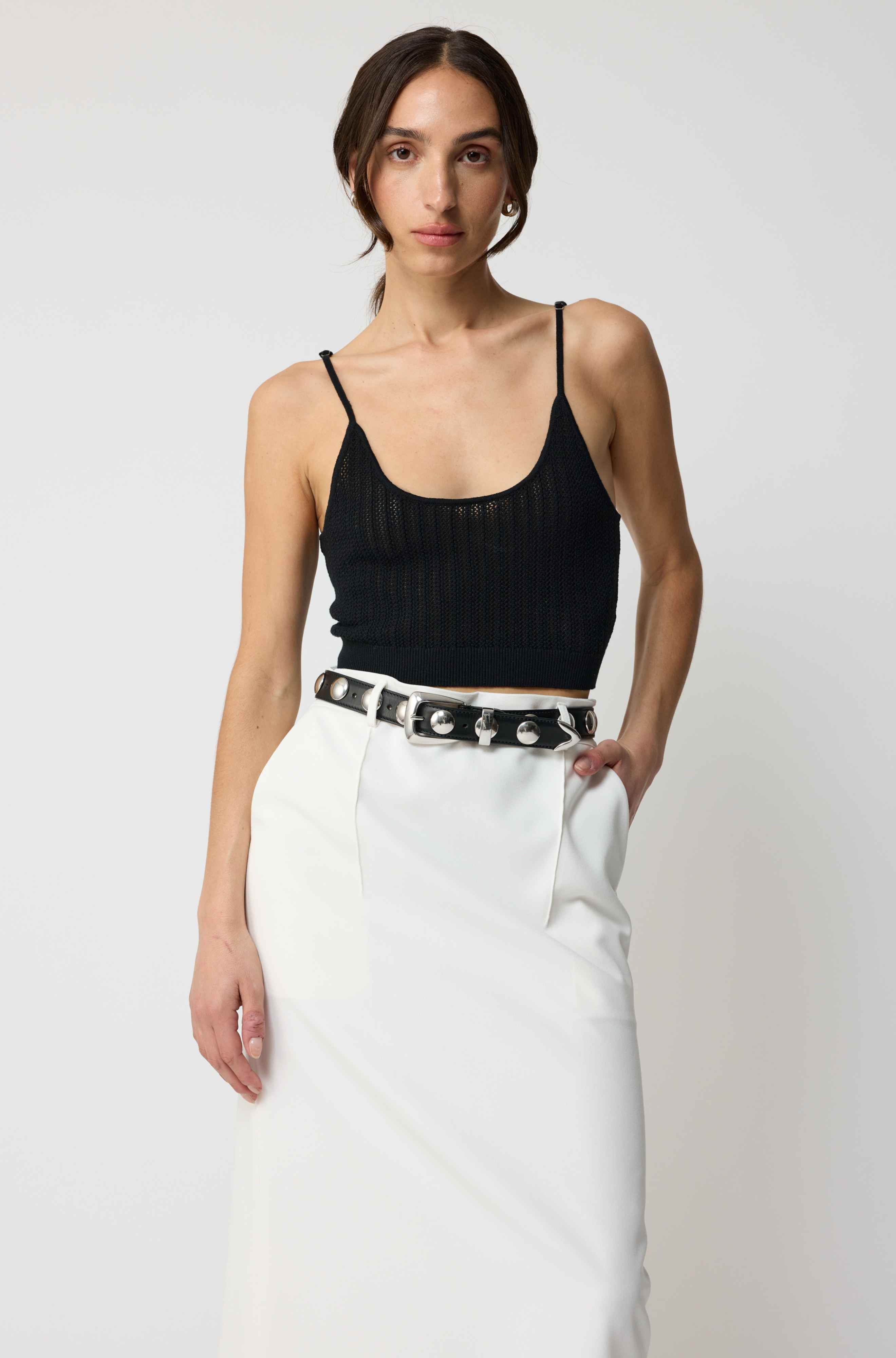 Woman wearing a black top and white pants with a belt on a plain background