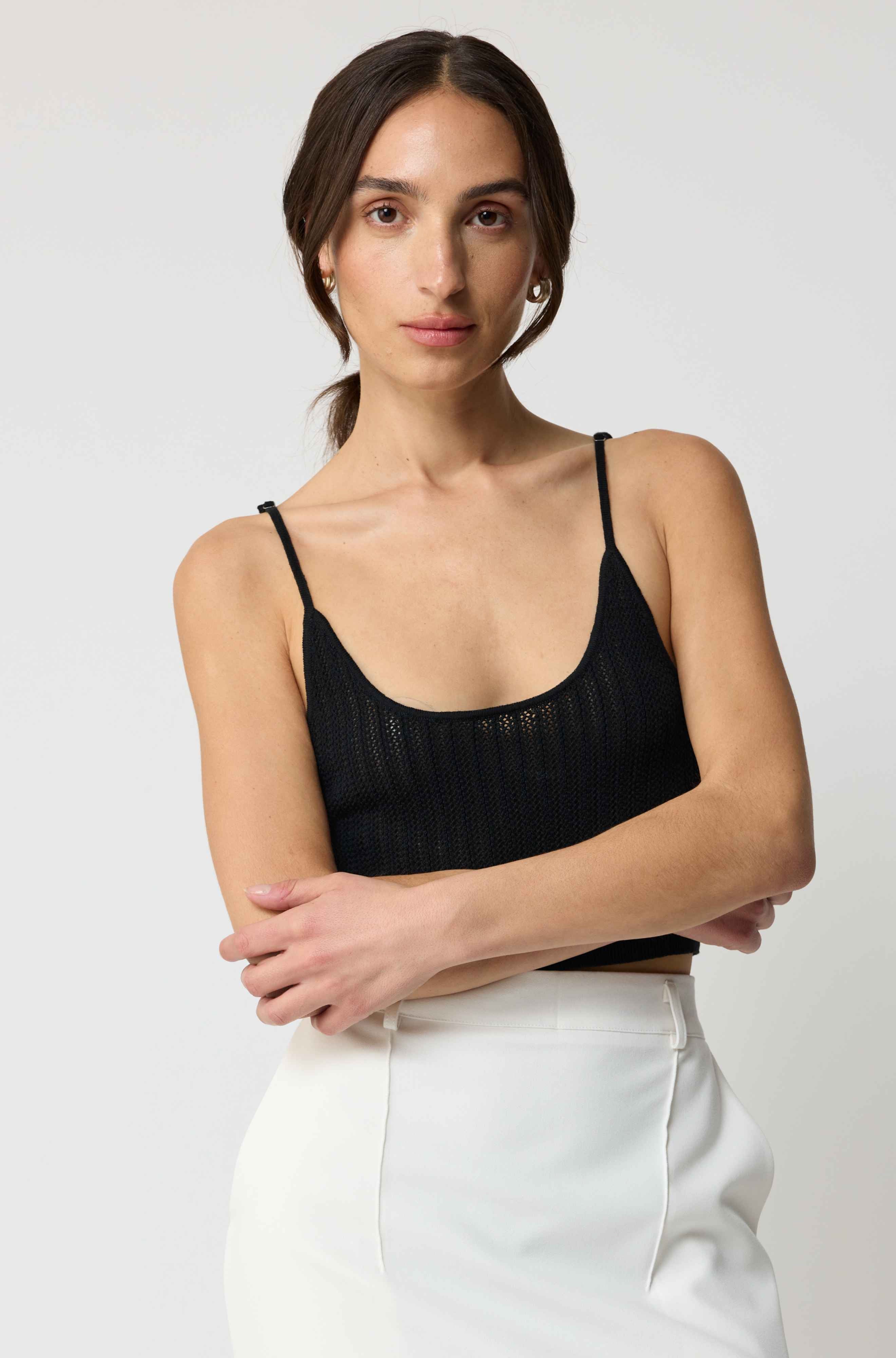 Woman wearing a black top and white pants against a plain background