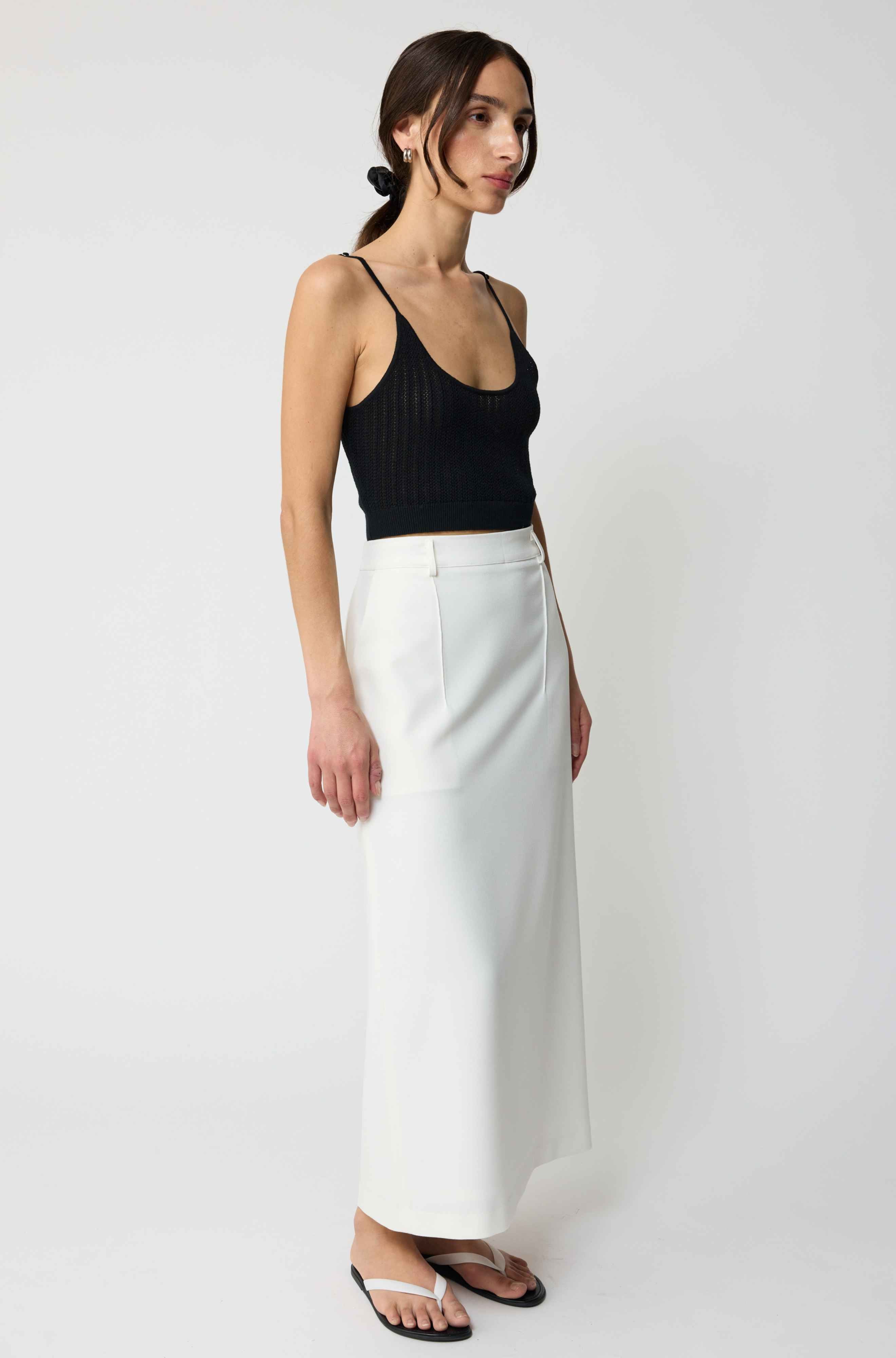 Woman wearing a black top and white pants on a white background