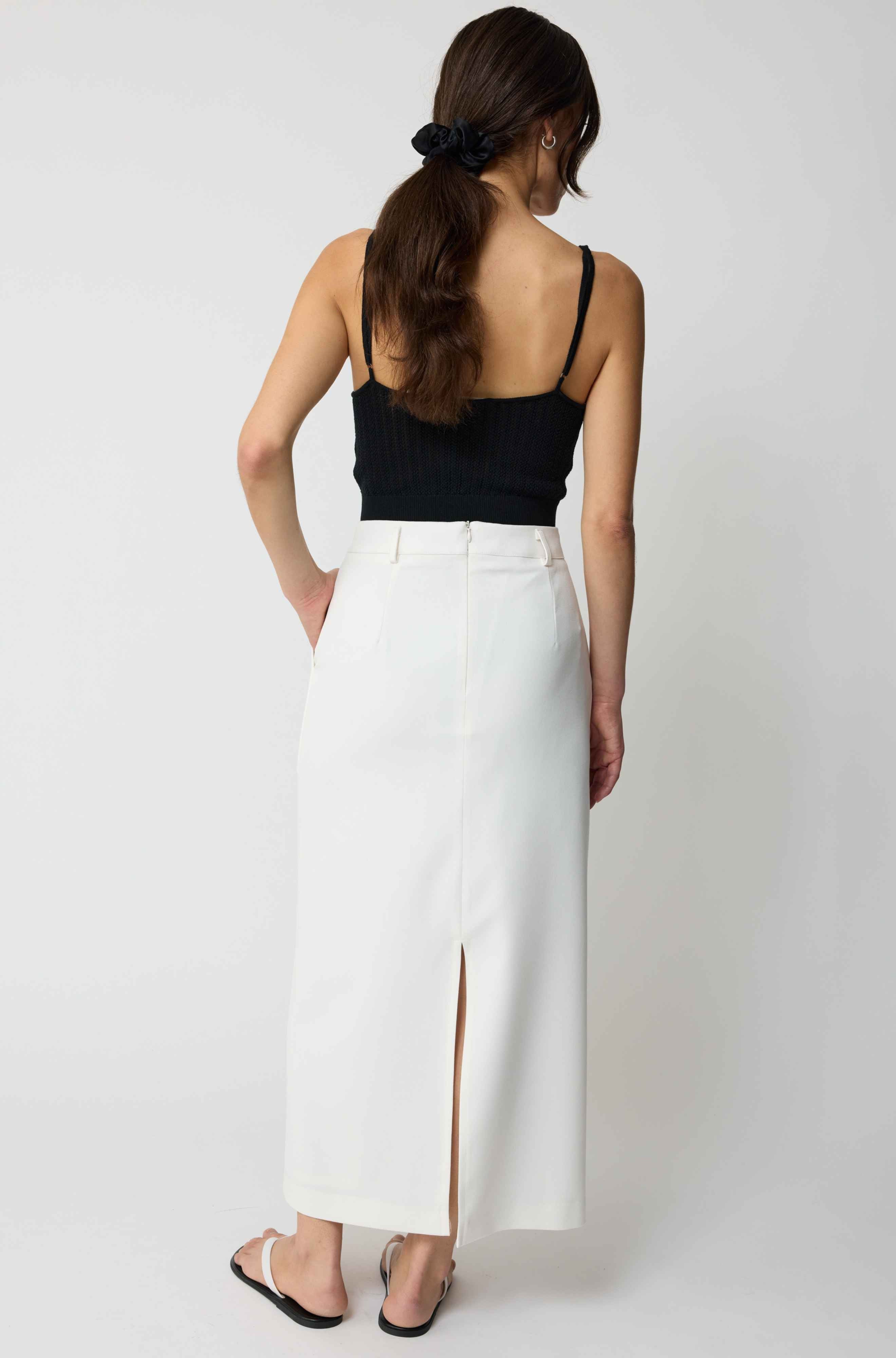 Woman wearing a black top and white pants on a plain background
