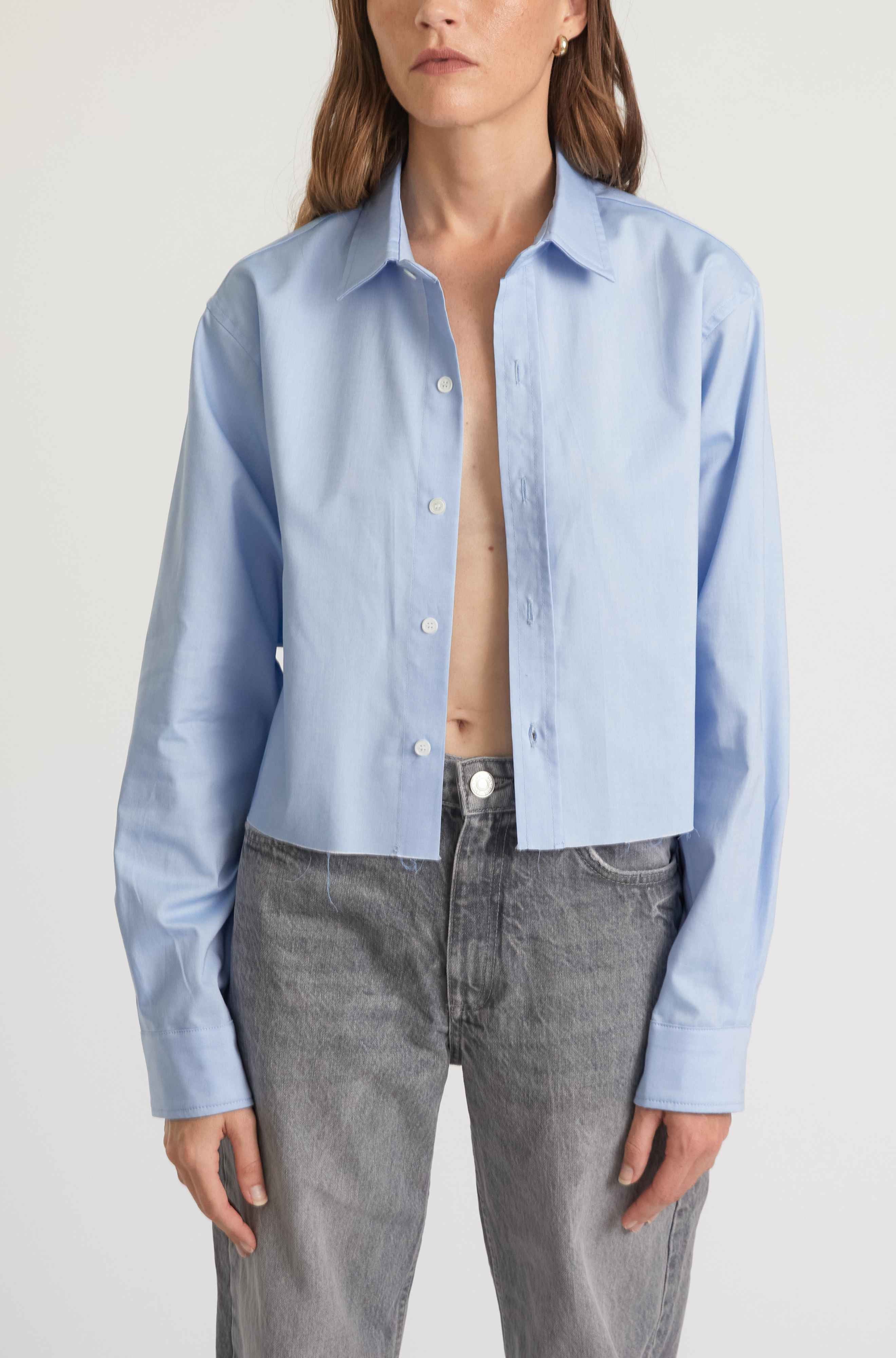 Person wearing a light blue button-up shirt and gray jeans on a white background