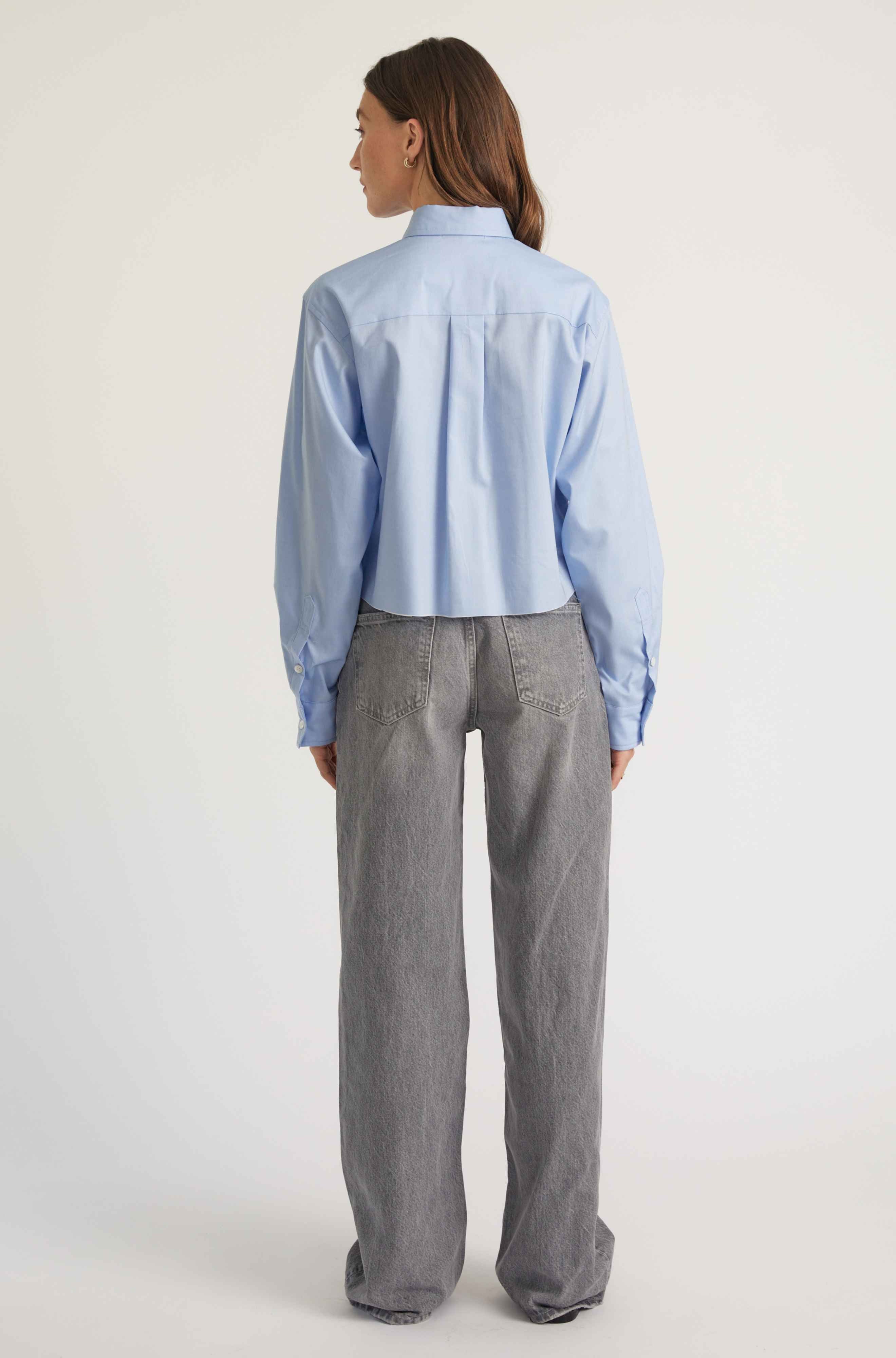 Person wearing a light blue shirt and gray pants on a white background