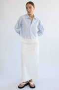 Woman wearing a light blue striped shirt and white skirt on a plain background
