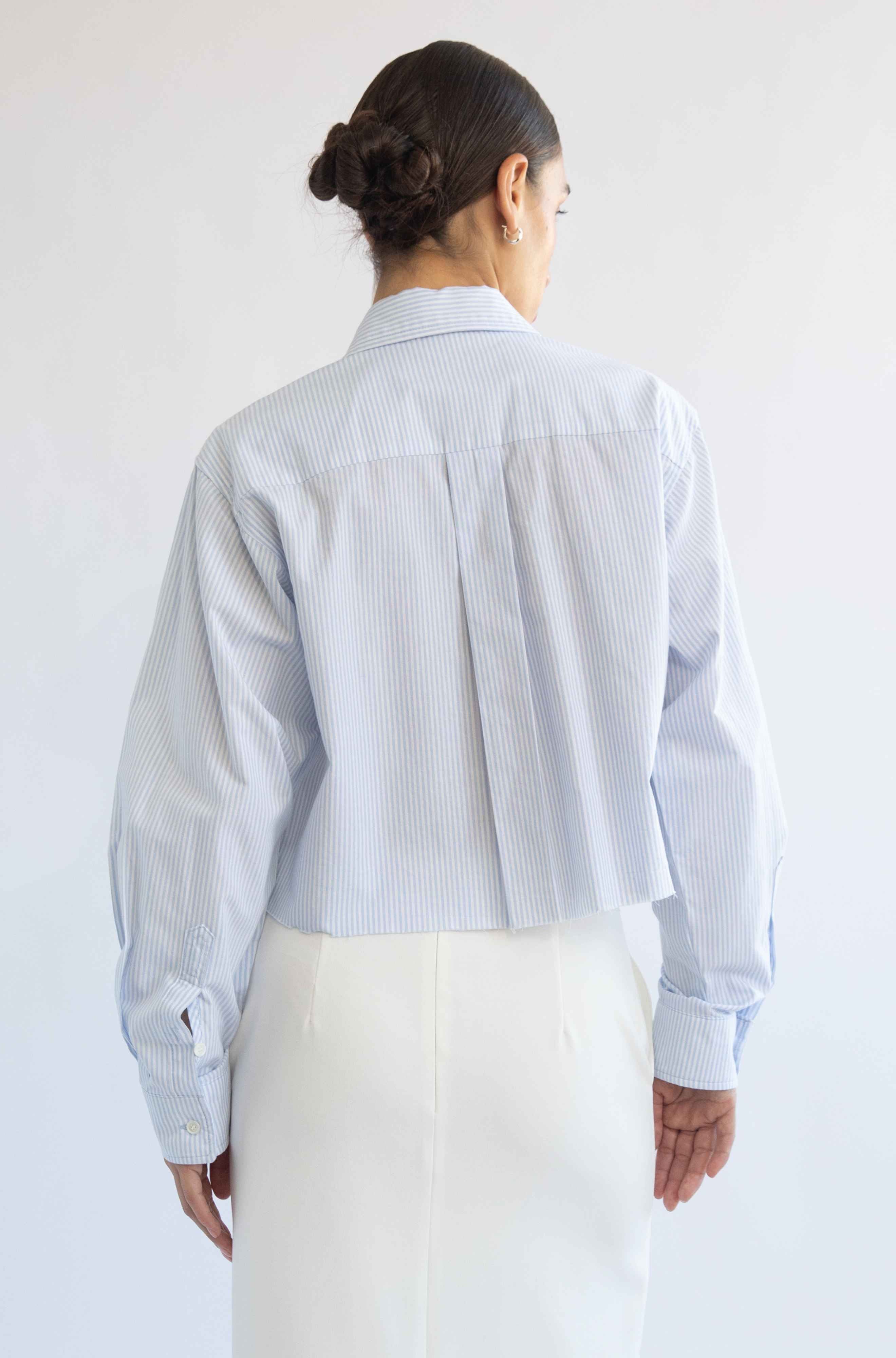 Person wearing a light blue striped shirt and white pants against a plain background