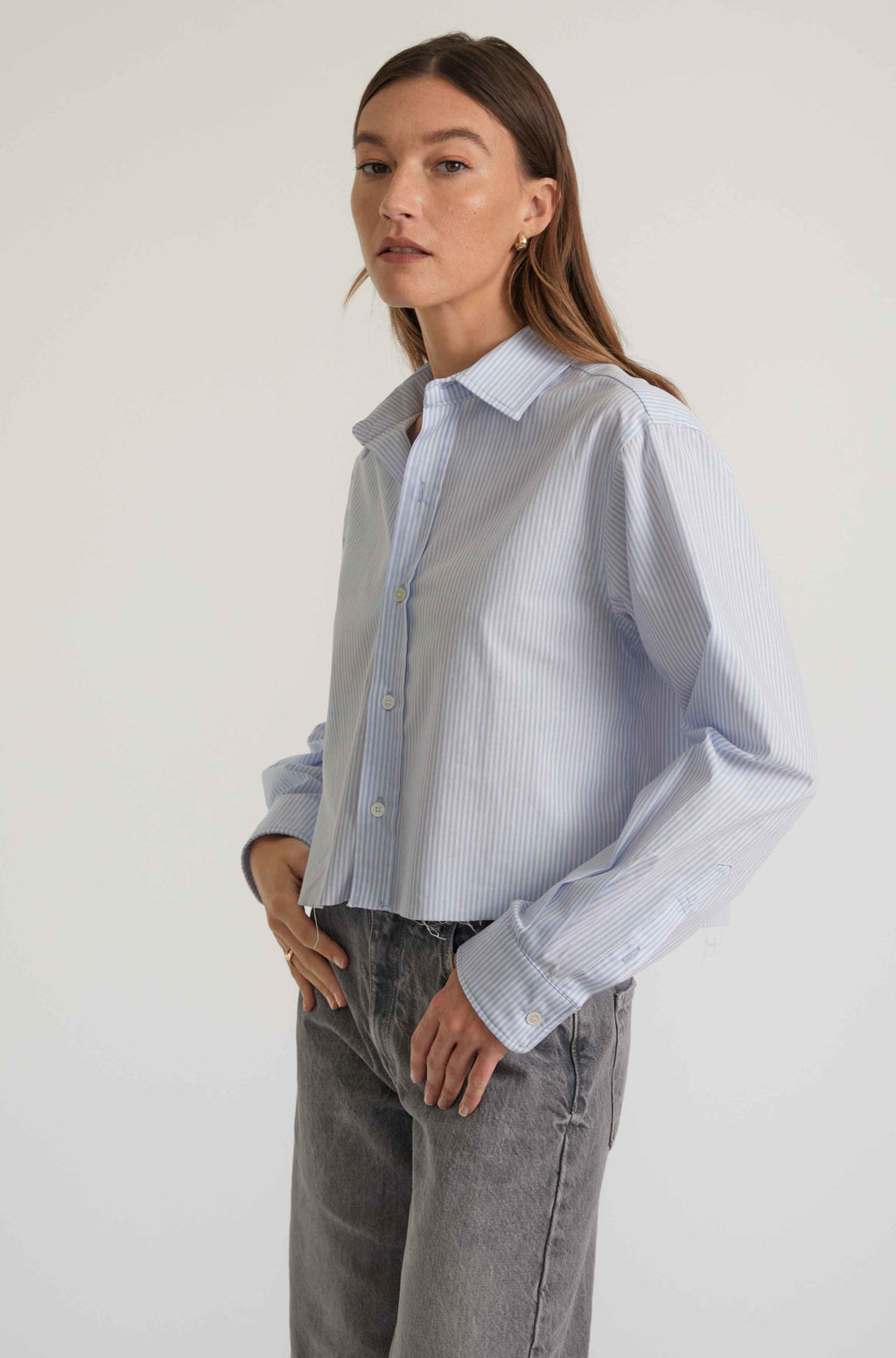 Woman wearing a light blue striped shirt and gray pants on a white background