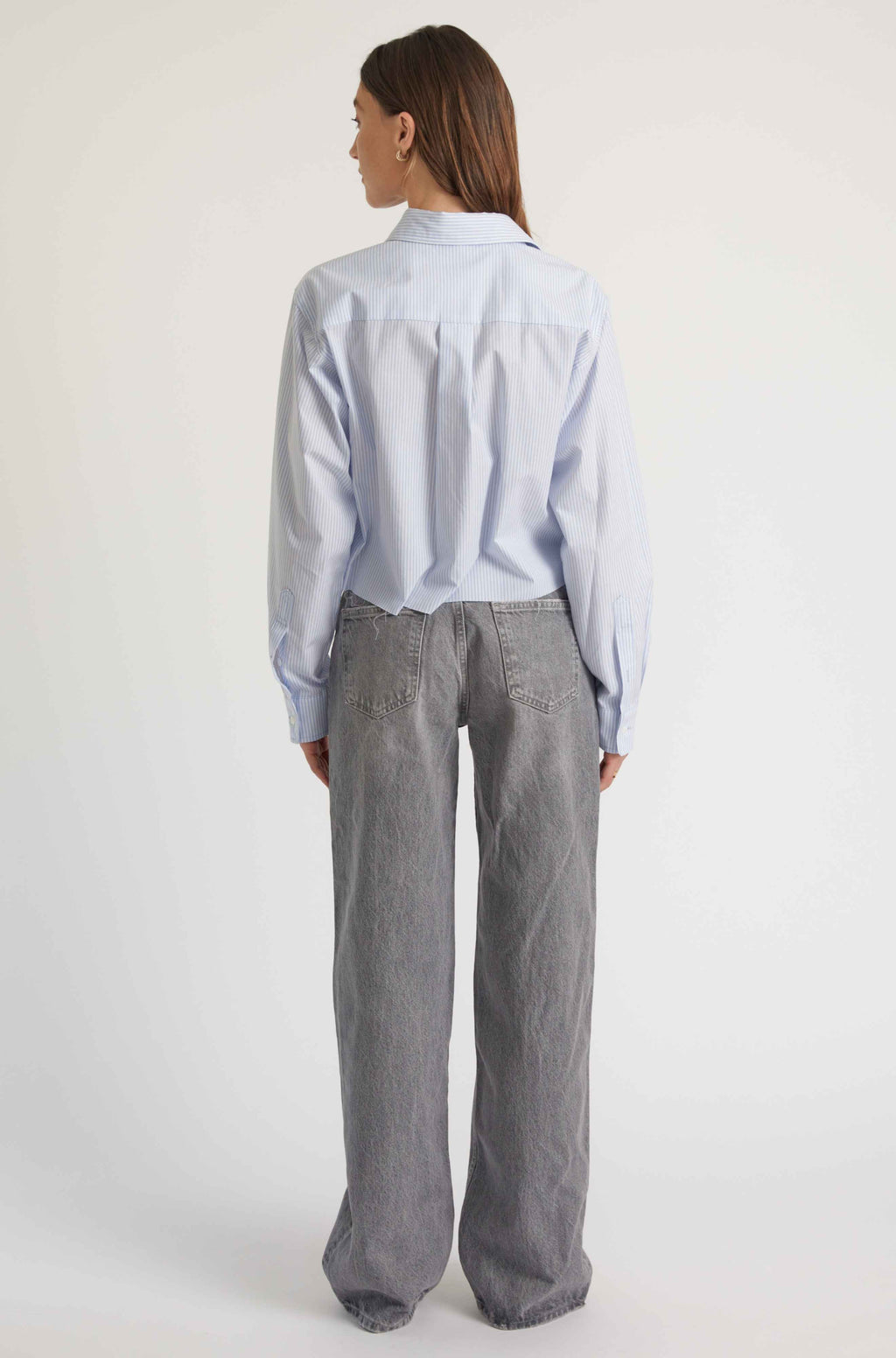 Person wearing a light blue shirt and gray pants on a white background