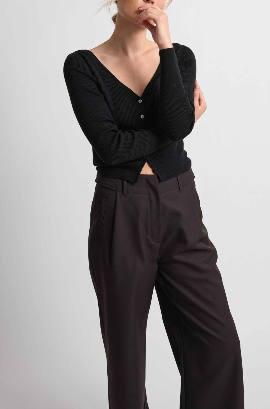 Person wearing a black long-sleeve top and dark pants on a light gray background