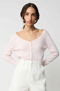 Woman wearing a light pink long-sleeve top and white pants on a plain background