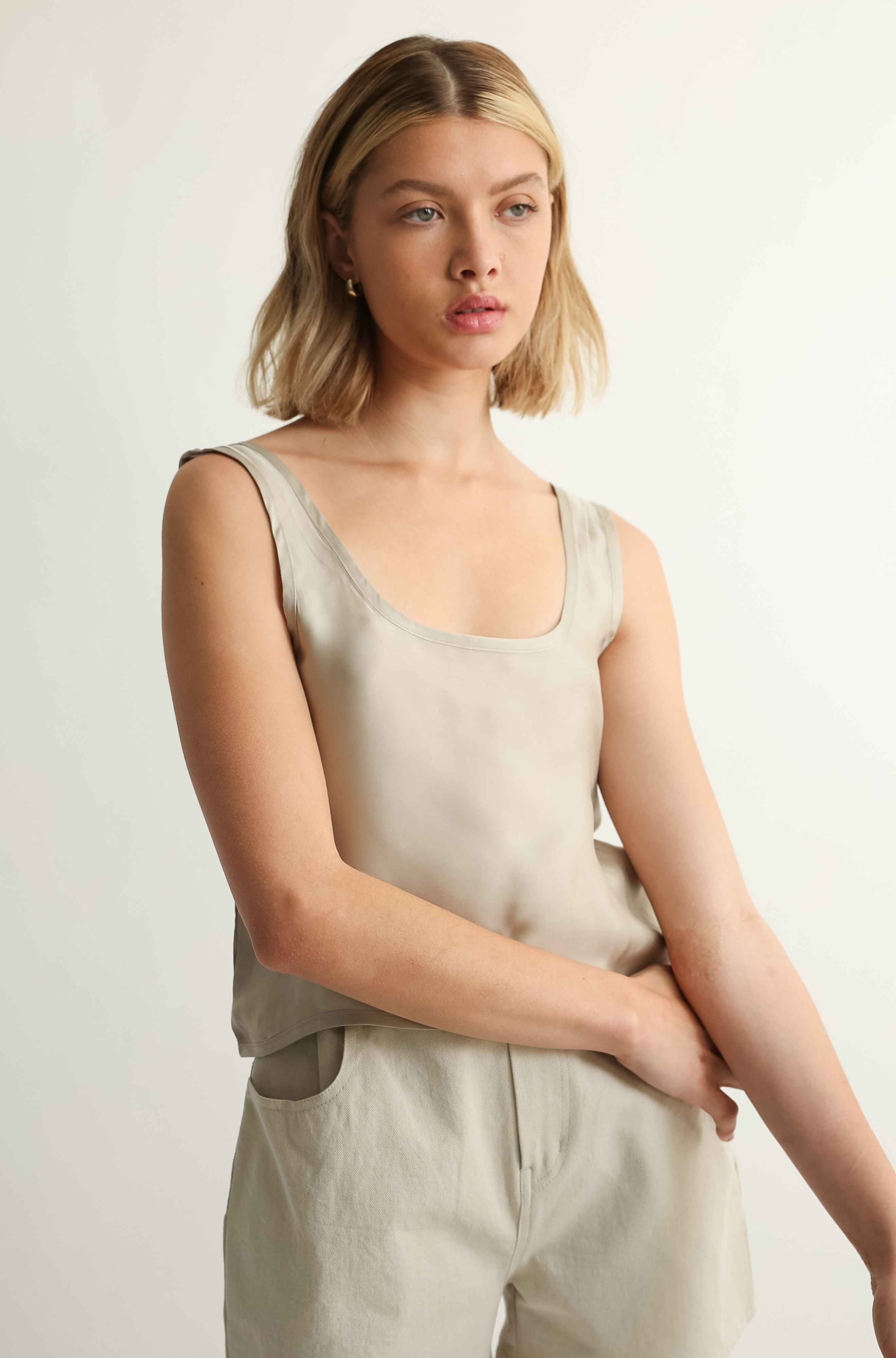 Woman wearing a beige sleeveless top and pants against a plain background