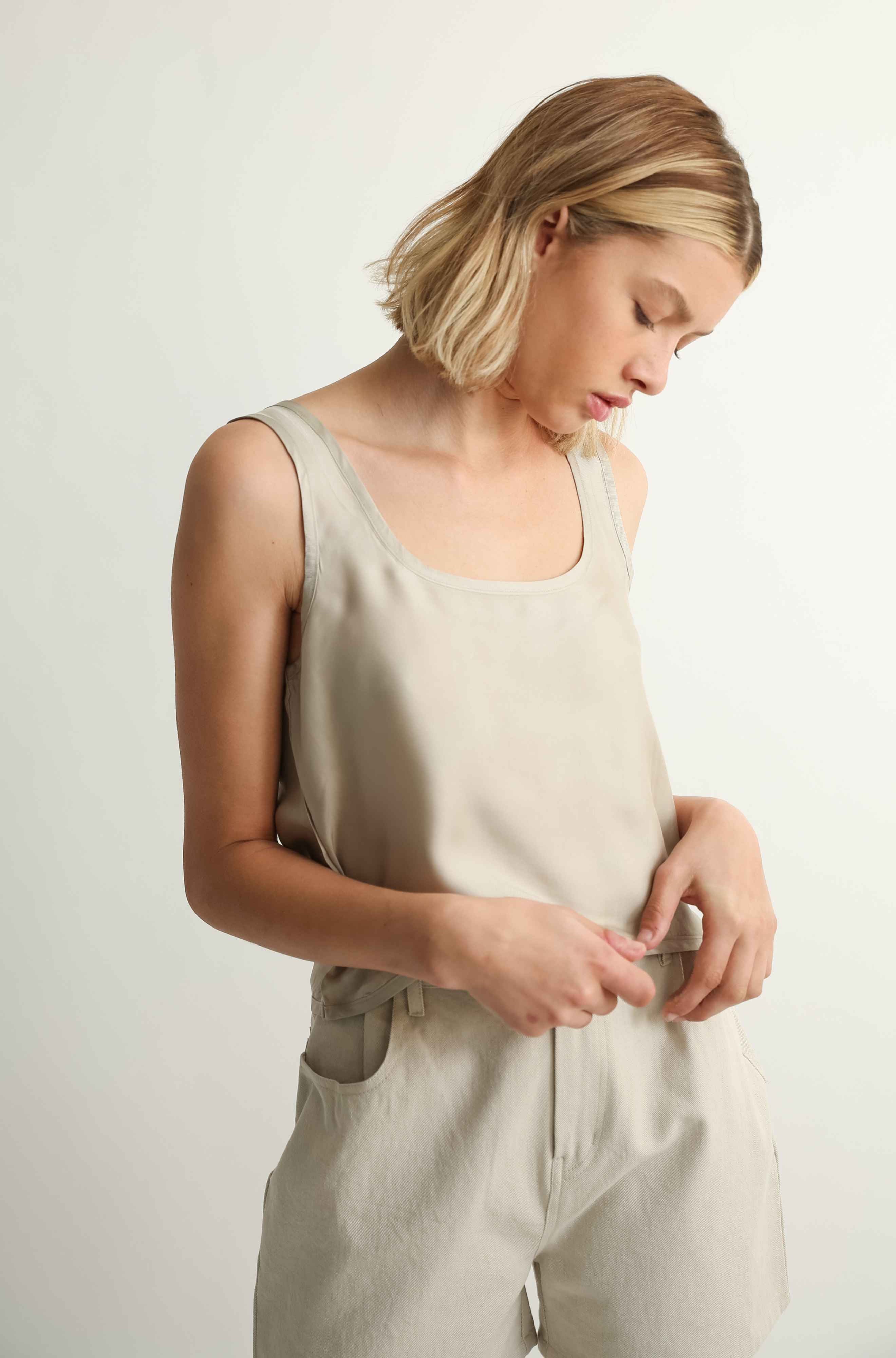 Woman wearing a beige sleeveless top and pants against a plain background