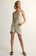 Woman wearing a silk top and beige shorts against a grey background
