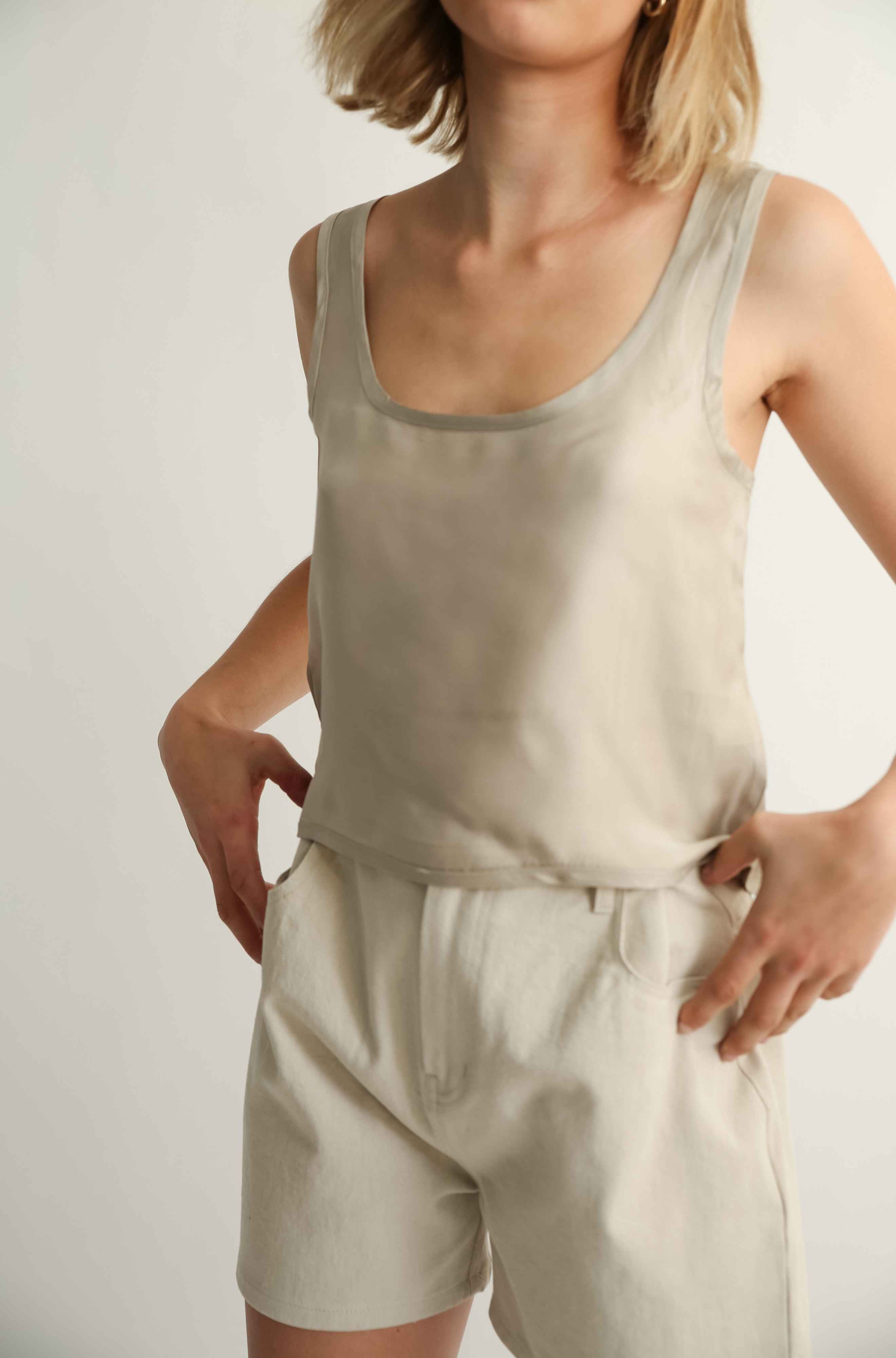 Woman wearing a silk top and beige shorts against a grey background