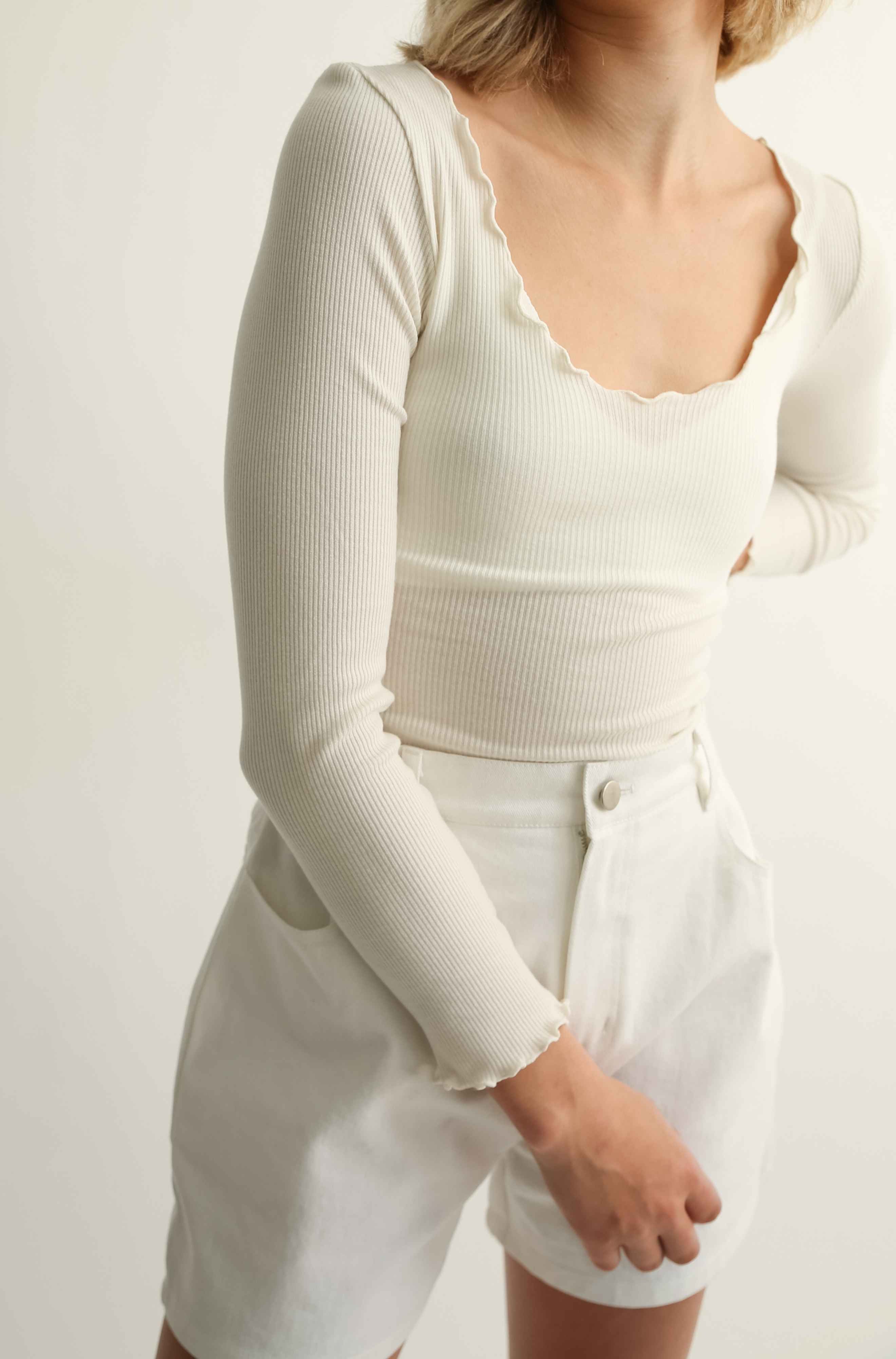 Woman wearing a long sleeve tee and white shorts against a plain background