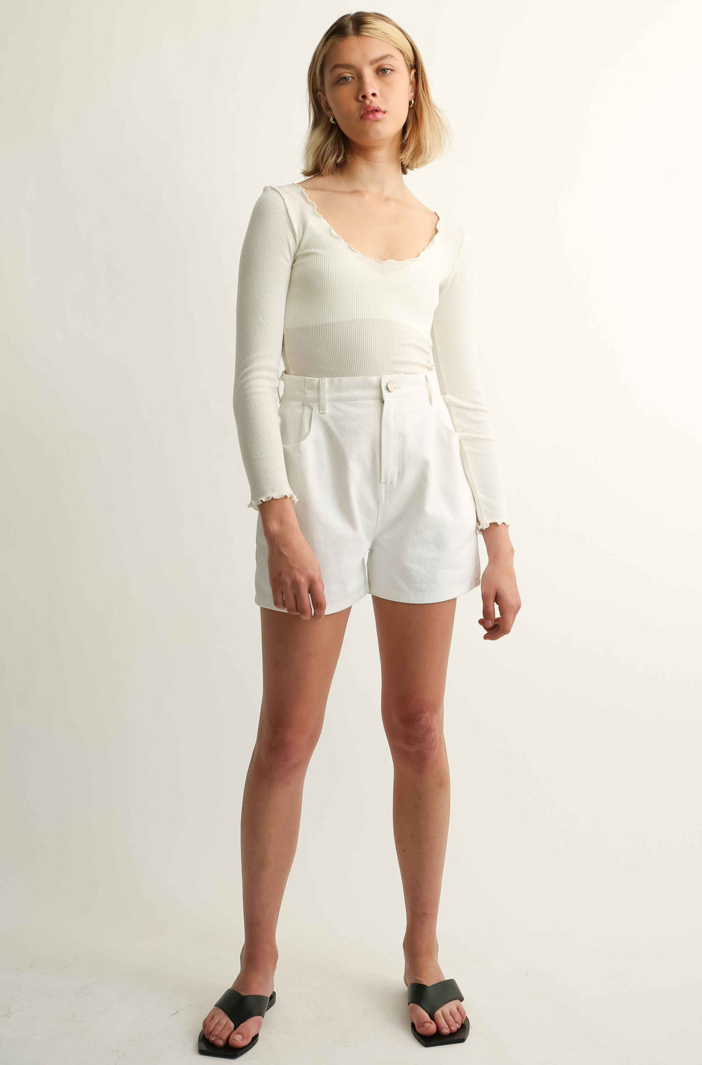 Woman wearing a long sleeve tee and white shorts against a plain background
