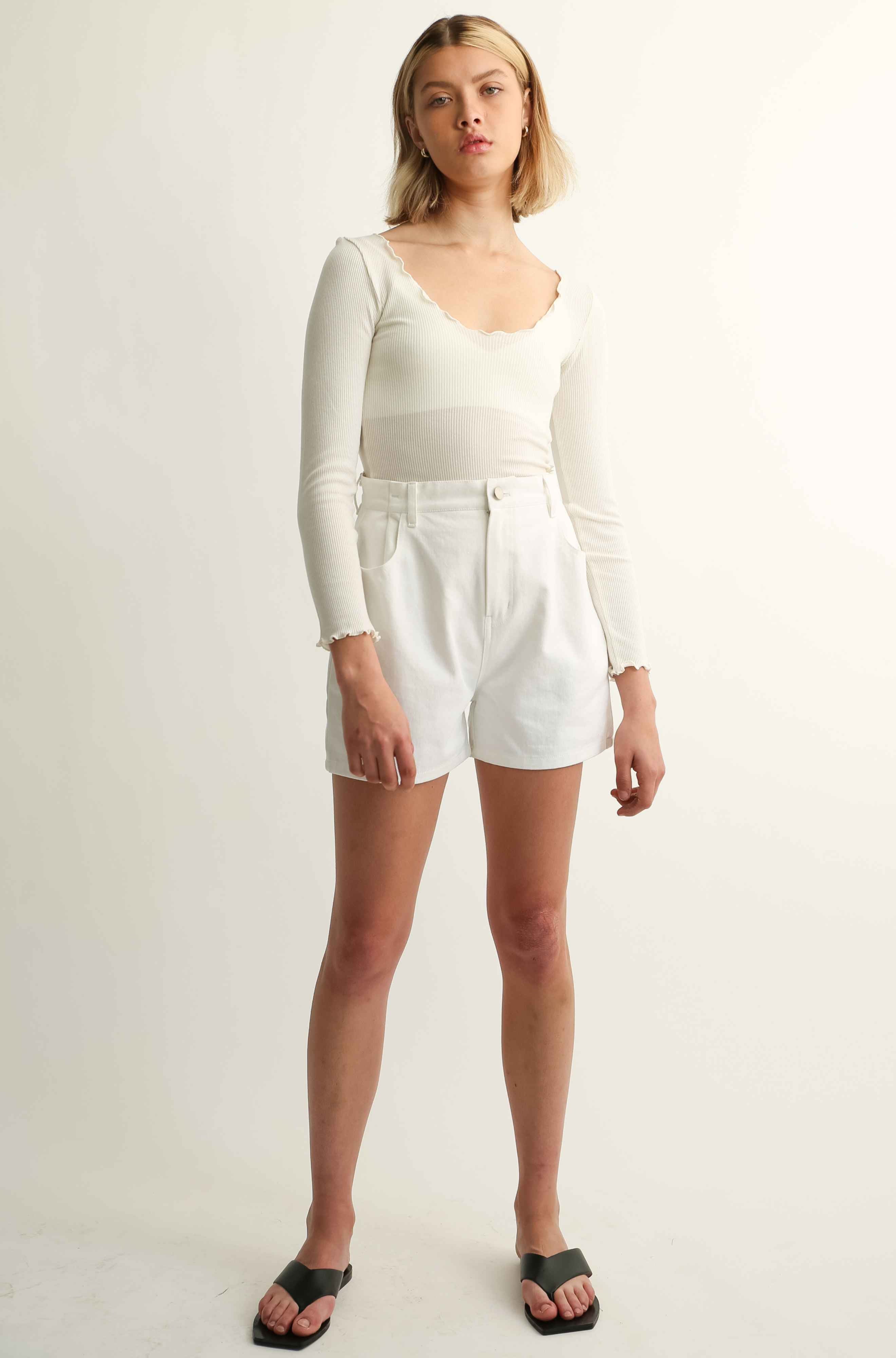 Woman wearing a long sleeve tee and white shorts against a plain background