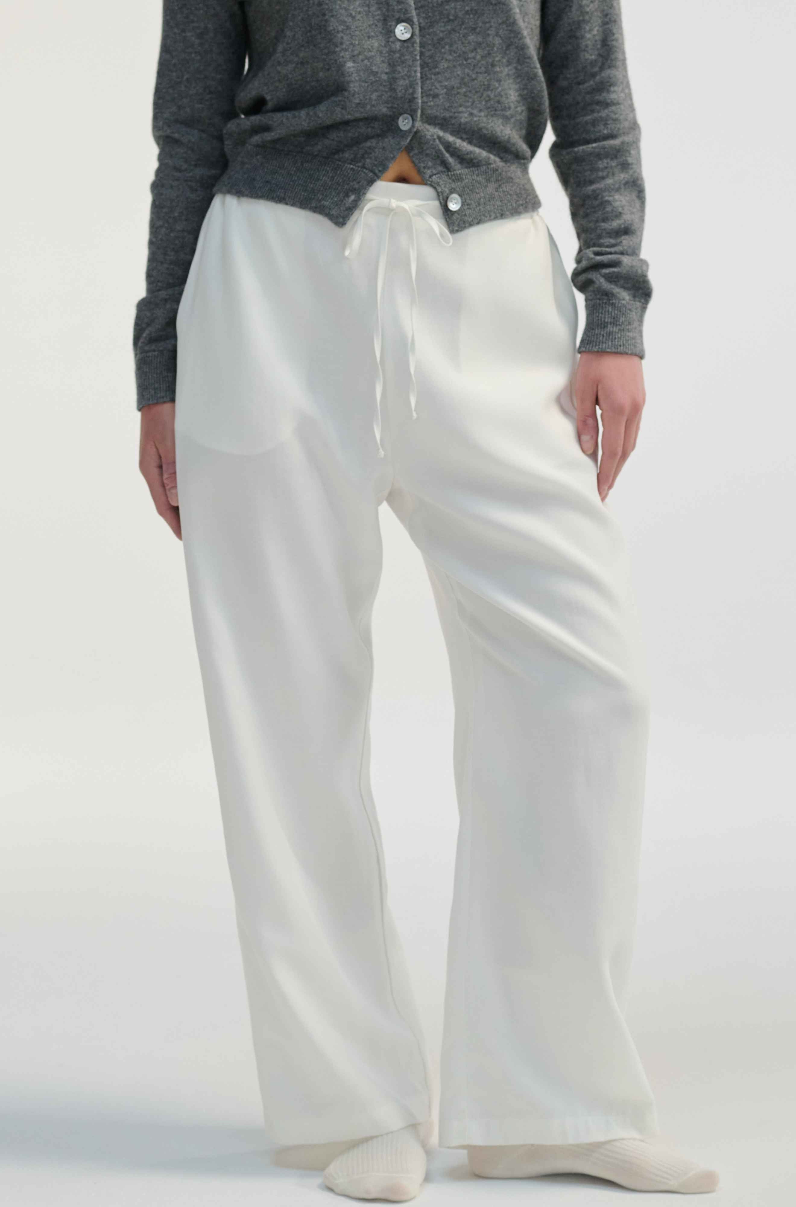 Woman wearing white linen pants on a light grey background