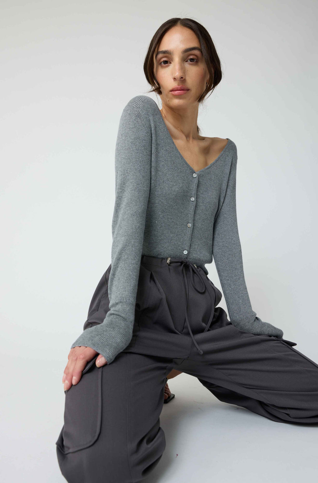 Woman wearing a grey cardigan with grey cargo pants on a light grey background
