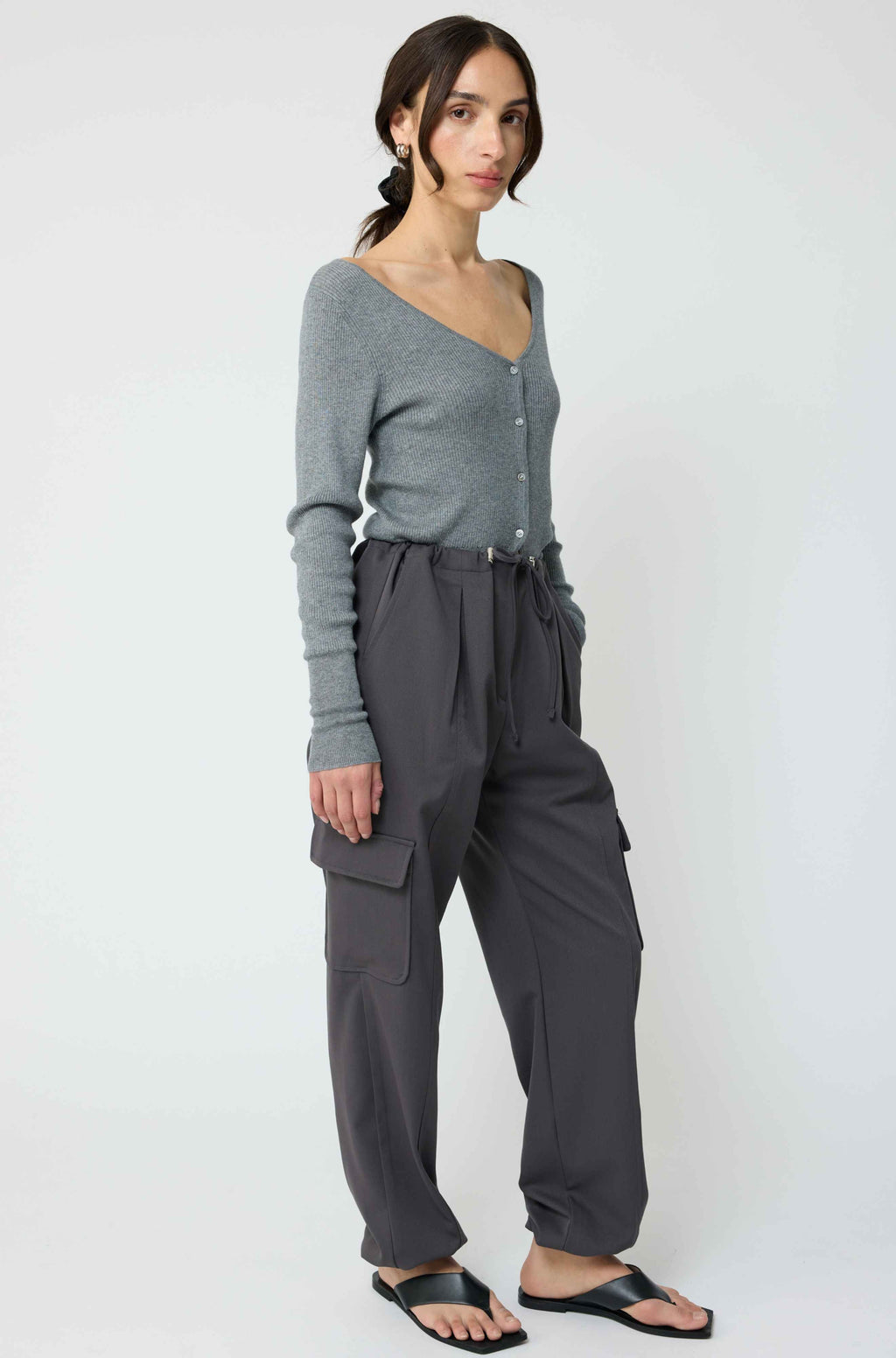 Woman wearing a grey cardigan with grey cargo pants on a light grey background