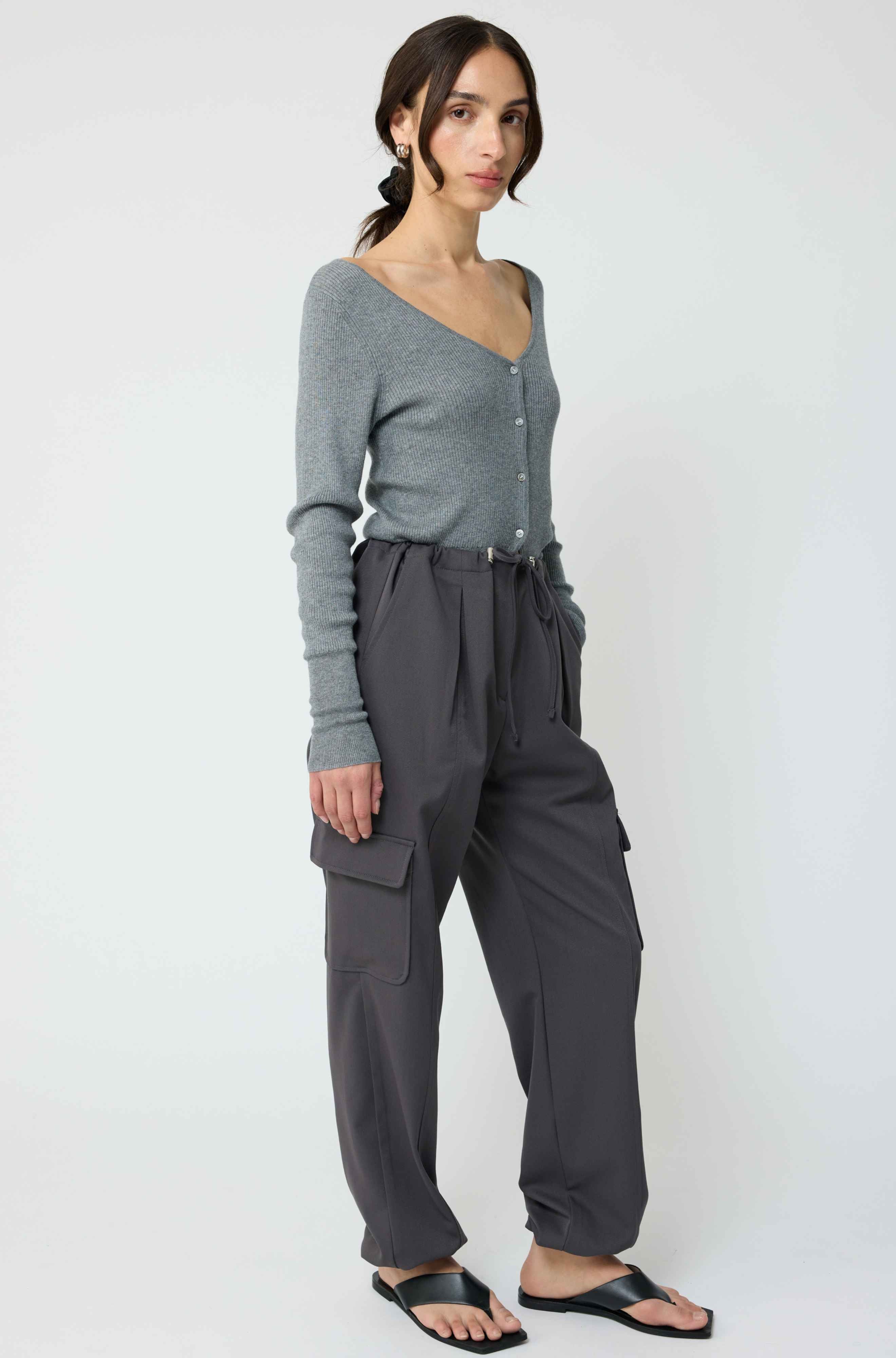 Woman wearing a grey cardigan with grey cargo pants on a light grey background