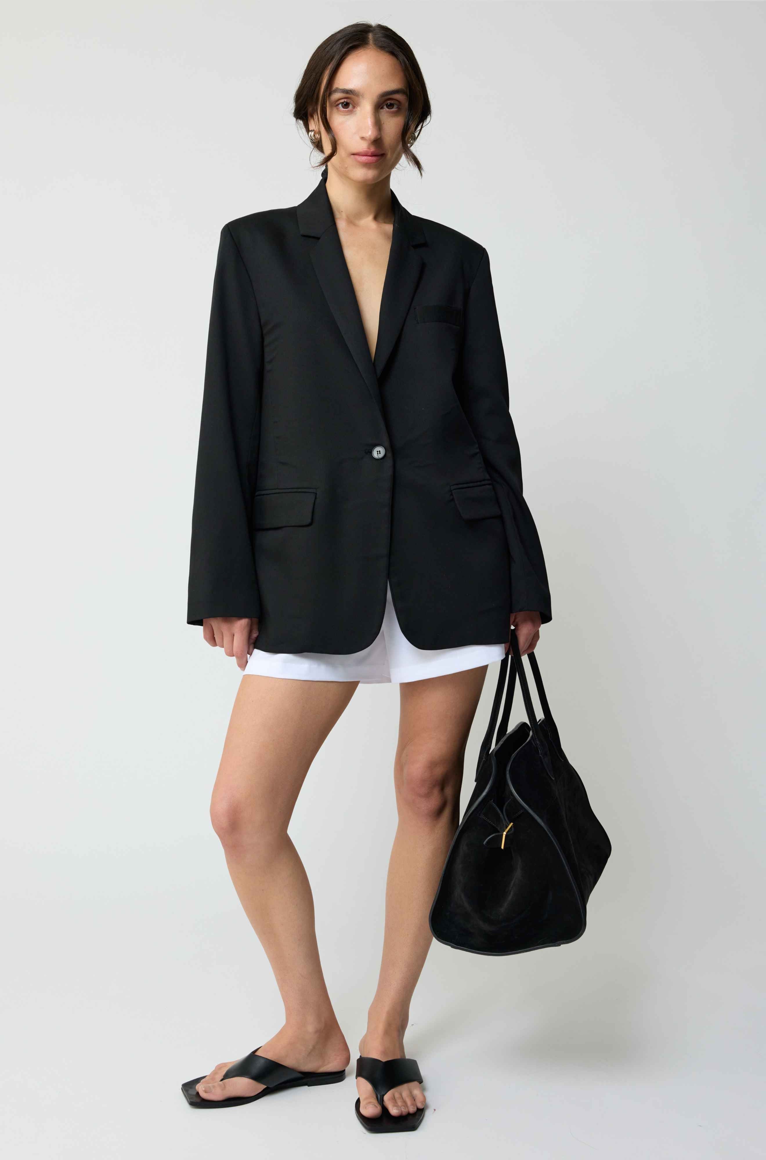 Woman wearing a black blazer over a white dress, holding a black handbag on a white background