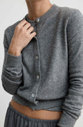 A close-up of a woman wearing a heather gray ribbed cardigan with front buttons, paired with gray bottoms, against a plain light background.