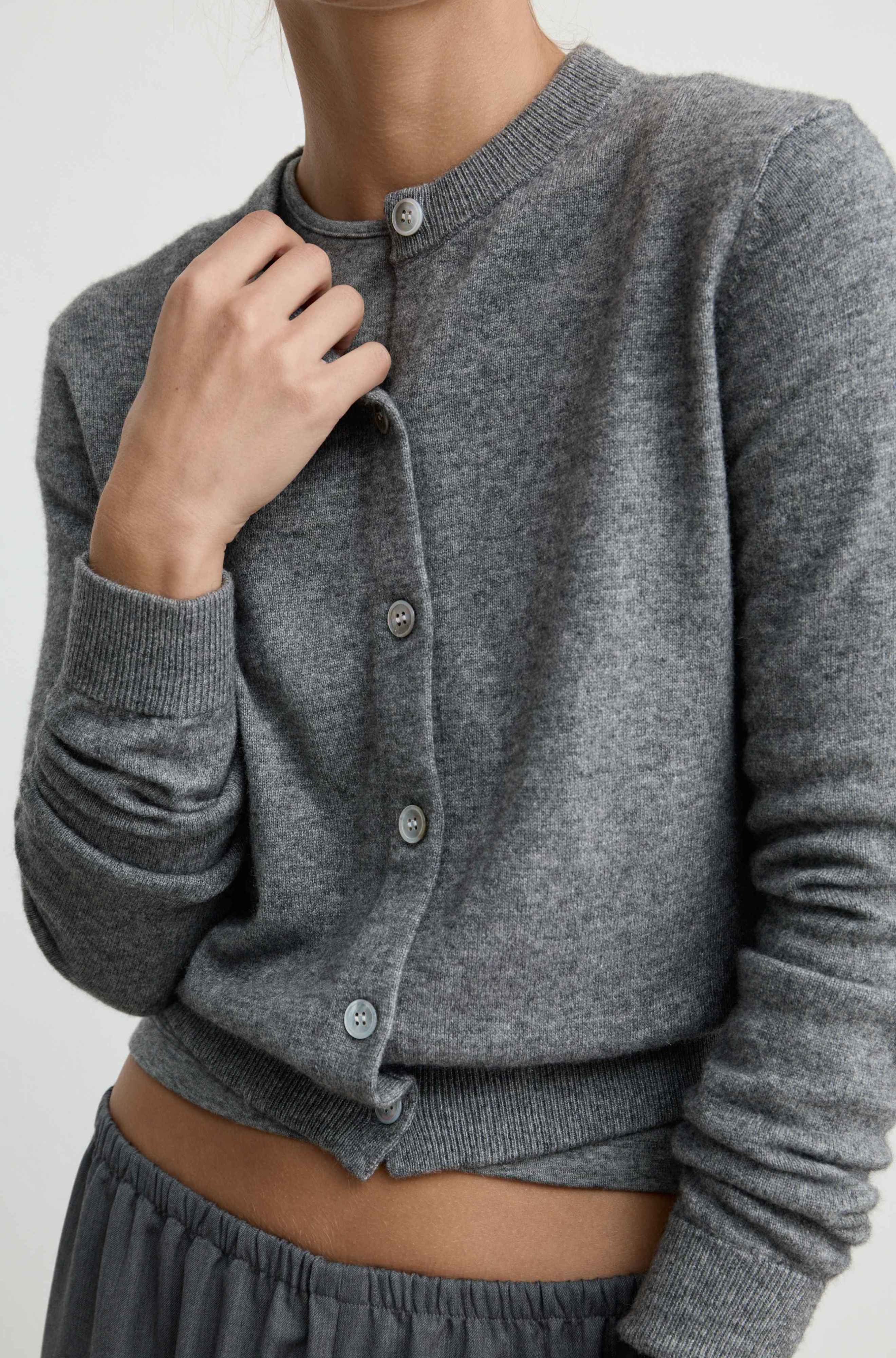 A close-up of a woman wearing a heather gray ribbed cardigan with front buttons, paired with gray bottoms, against a plain light background.