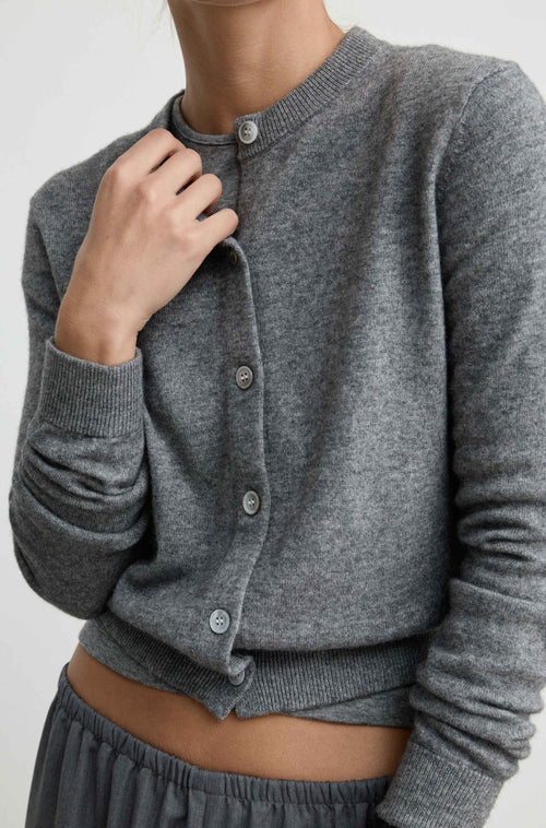 A close-up of a woman wearing a heather gray ribbed cardigan with front buttons, paired with gray bottoms, against a plain light background.