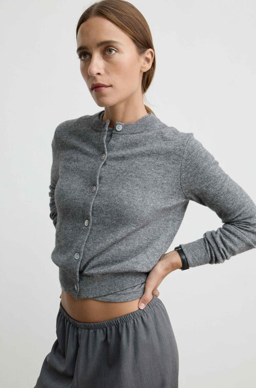 A woman wearing a gray long-sleeve button-front cardigan and matching gray pants, photographed against a plain light gray studio background.