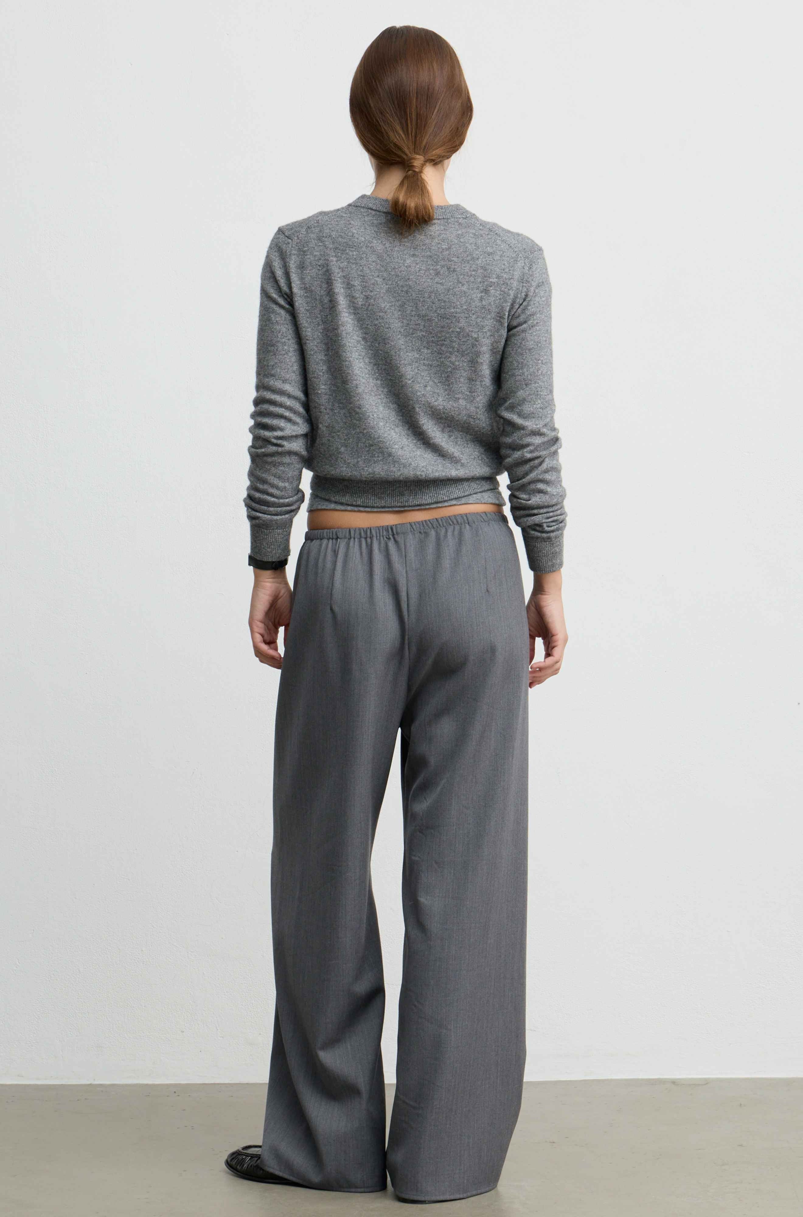 A model viewed from the back wearing a gray long-sleeve cropped sweater and matching wide-leg trousers against a plain light gray studio background.