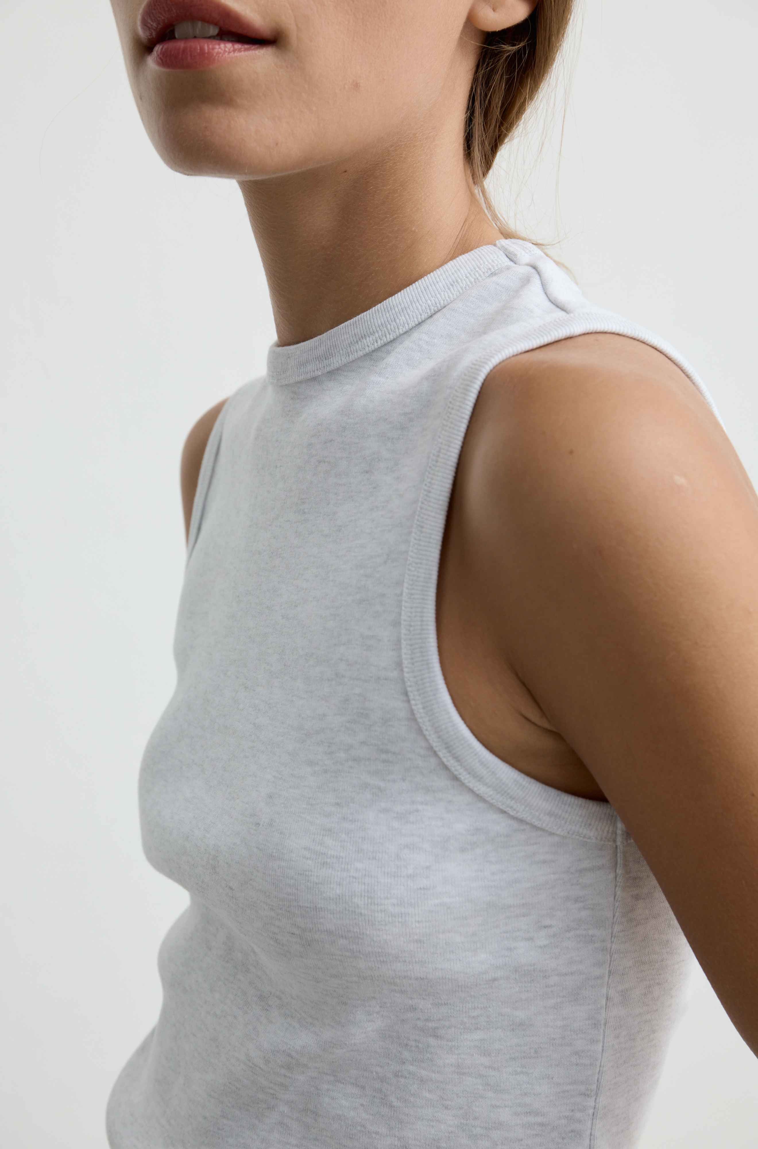Close-up of a model wearing a light gray sleeveless mock-neck tank top against a plain light background.