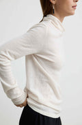 A woman wearing a cream-colored, long-sleeve turtleneck knit sweater, shown from a side-back angle against a plain white studio background.